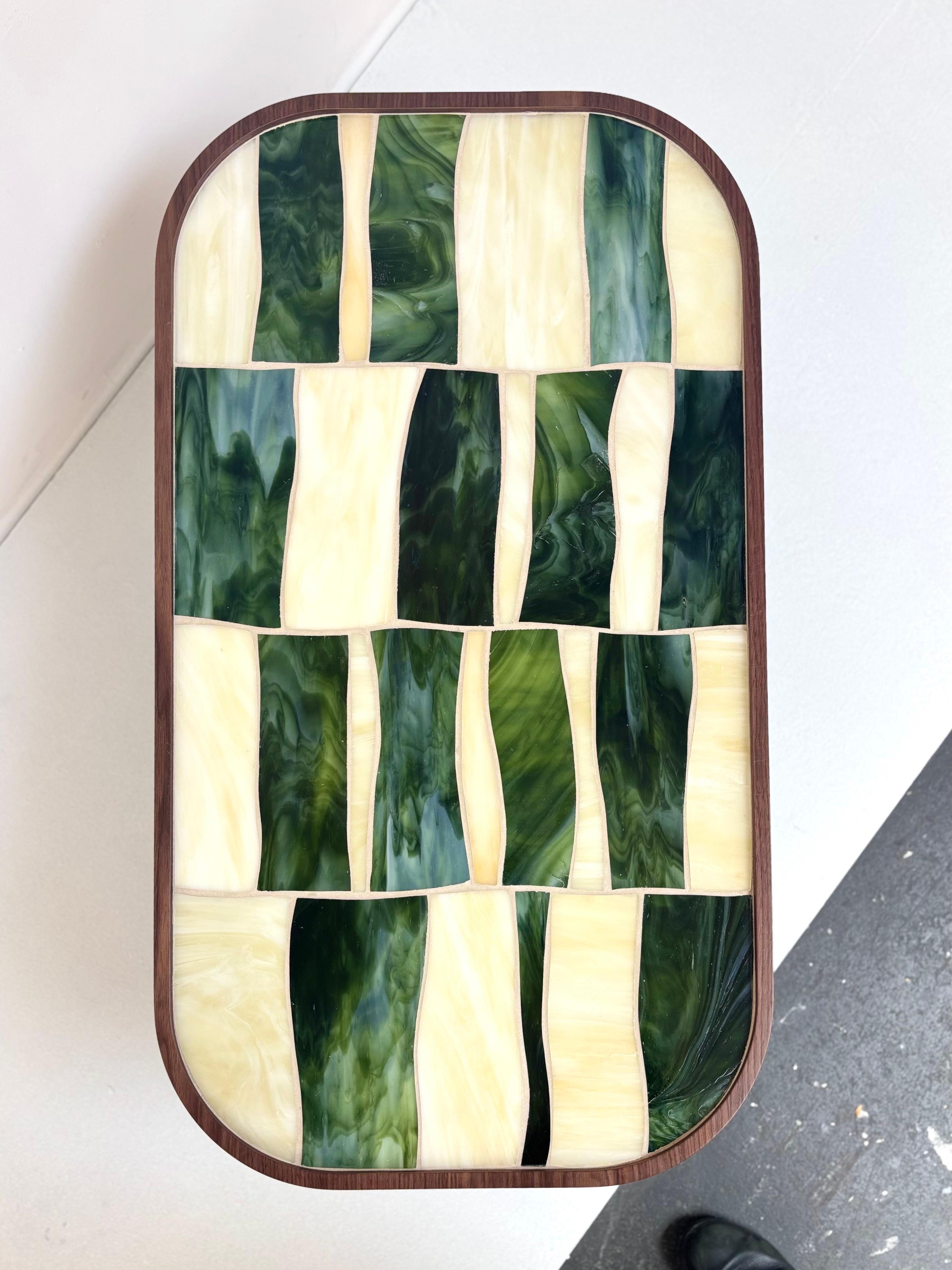 Palazzo oval coffee table with green and ivory glass sits on 1 Walnut Wood pedestal by Ercole Home. 

A sleek table with high craftsmanship and flowing mosaic patterns. The ivory and green glass is embedded into carved out refined walnut wood.