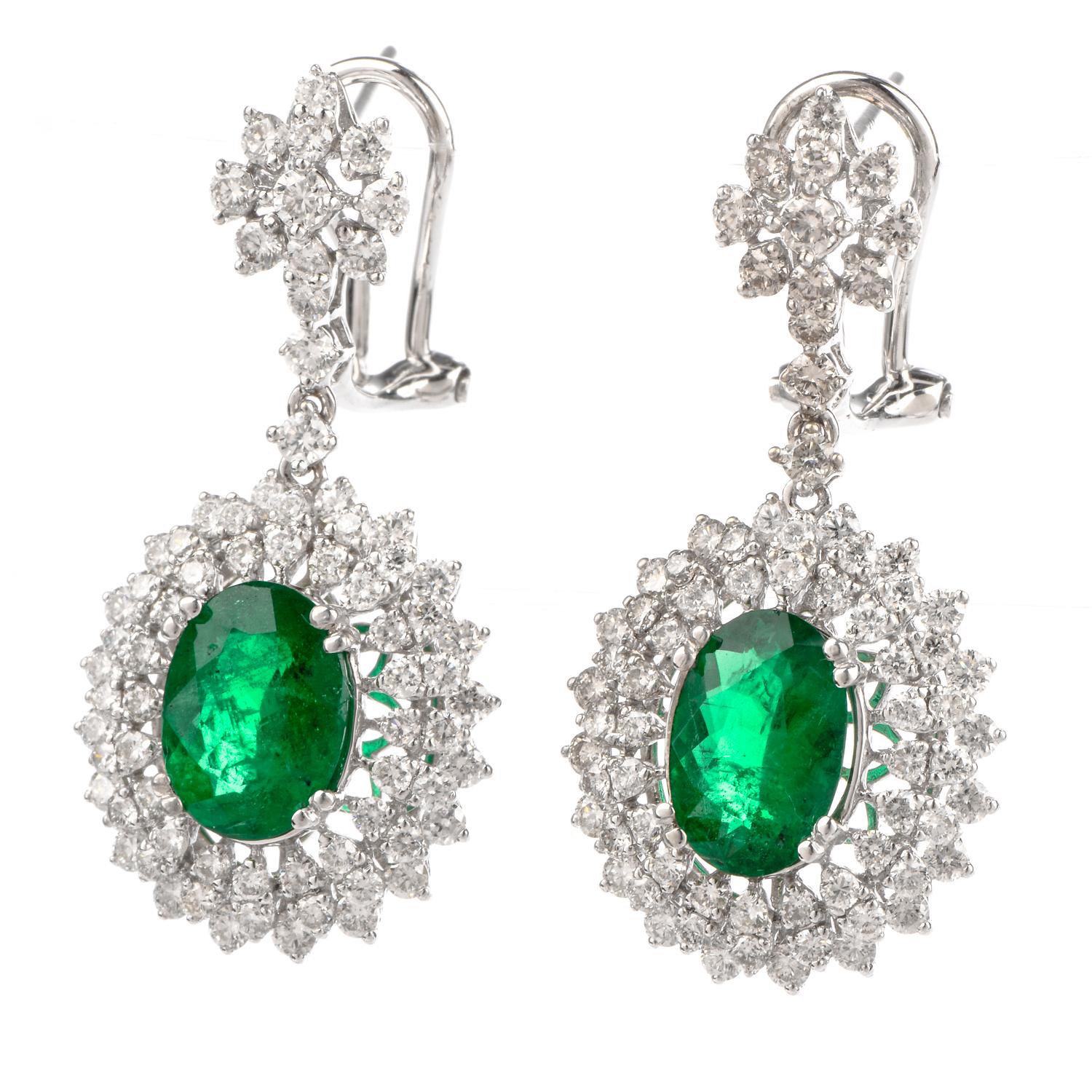 These stunning diamond and emerald dangle drop earrings are crafted in solid 18 karat white gold. Displaying a pair of prominent oval shaped prong-set emeralds, collectively weighing, 3.02 carats. Surrounded by a approx. 146 round-cut diamonds,