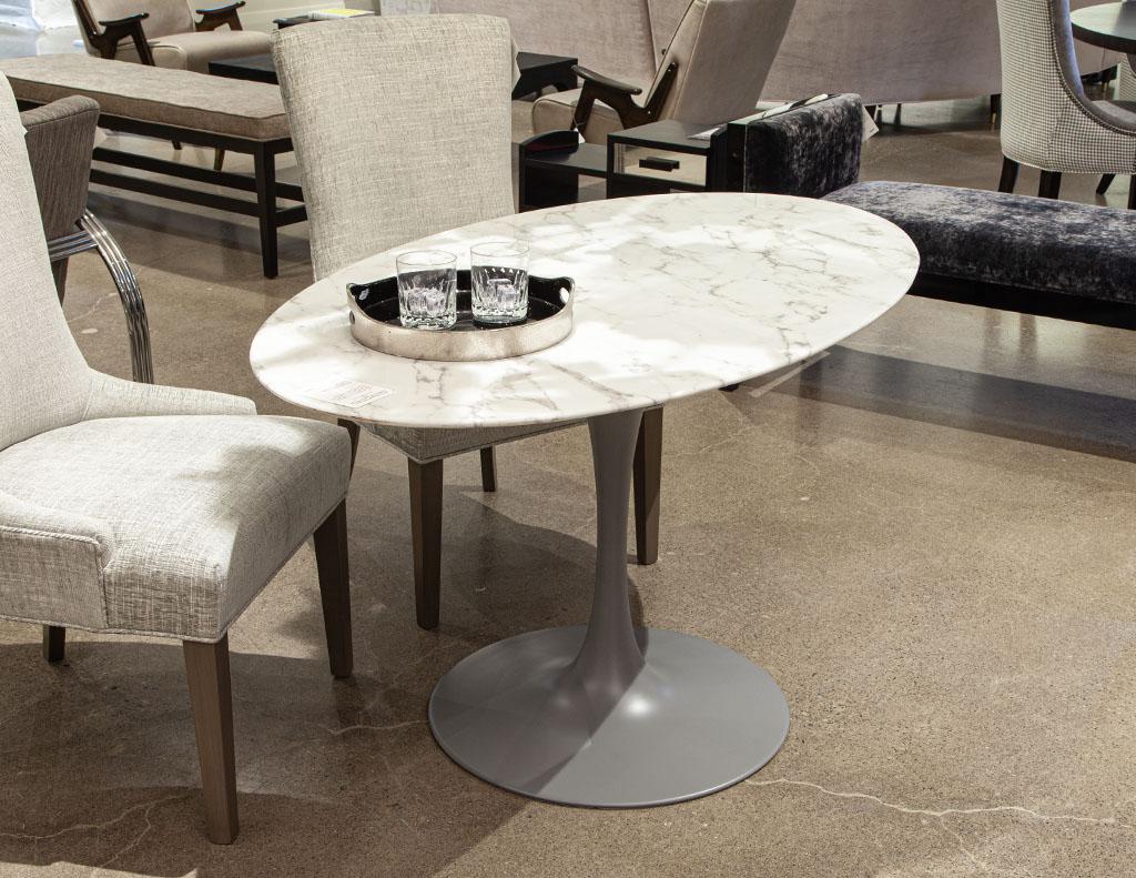 Modern oval marble top table in the style of Eero Saarinen Pedestal table. Beautiful Italian marble in white with rustic grey veining. Completed with a metal trumpet pedestal in a satin grey lacquered finish. Price includes complimentary curb side