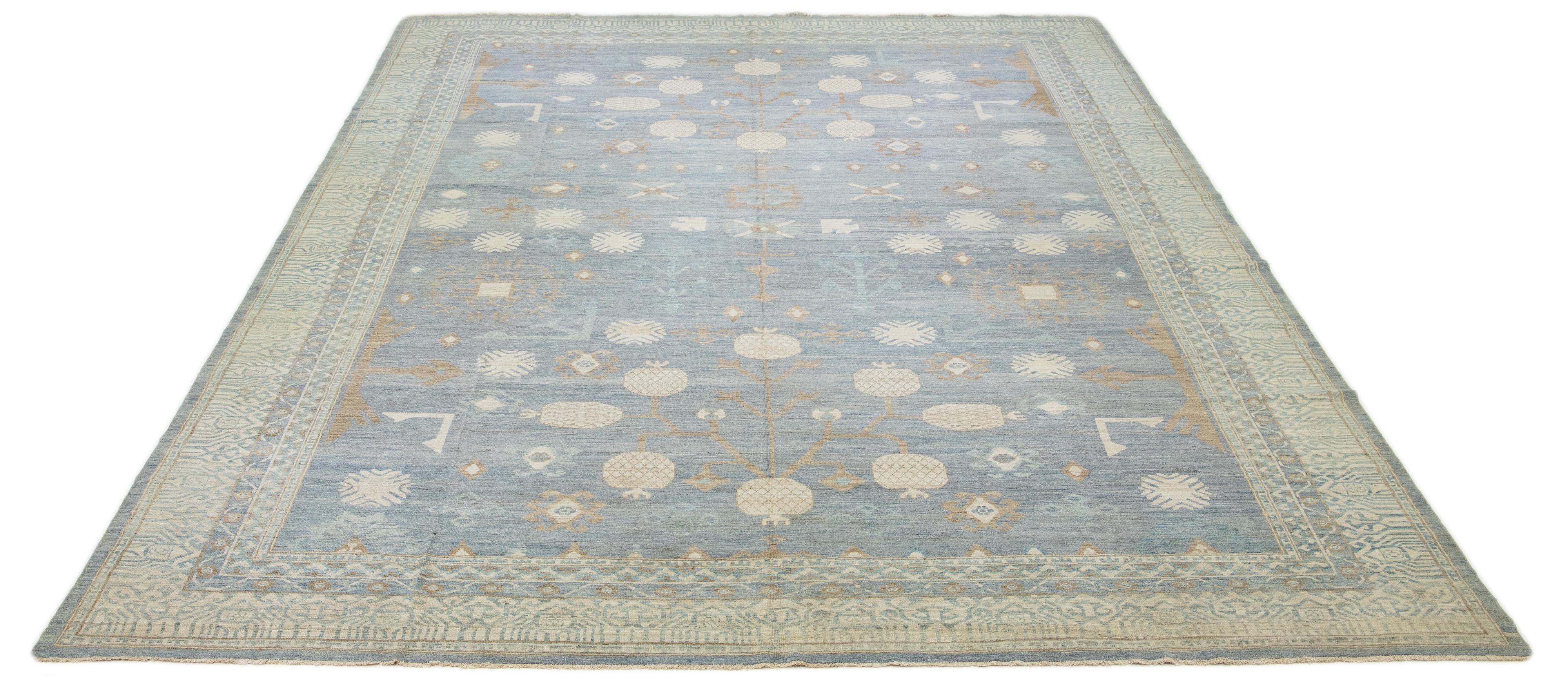 Dies ist ein übergroßer zeitgenössischer Khotan-Wollteppich aus Indien. Das Design zeigt eine hellblaue Basis mit verschlungenen braunen und cremefarbenen Mustern, darunter ein auffälliges, miteinander verbundenes Granatapfel-Rosettenmuster von