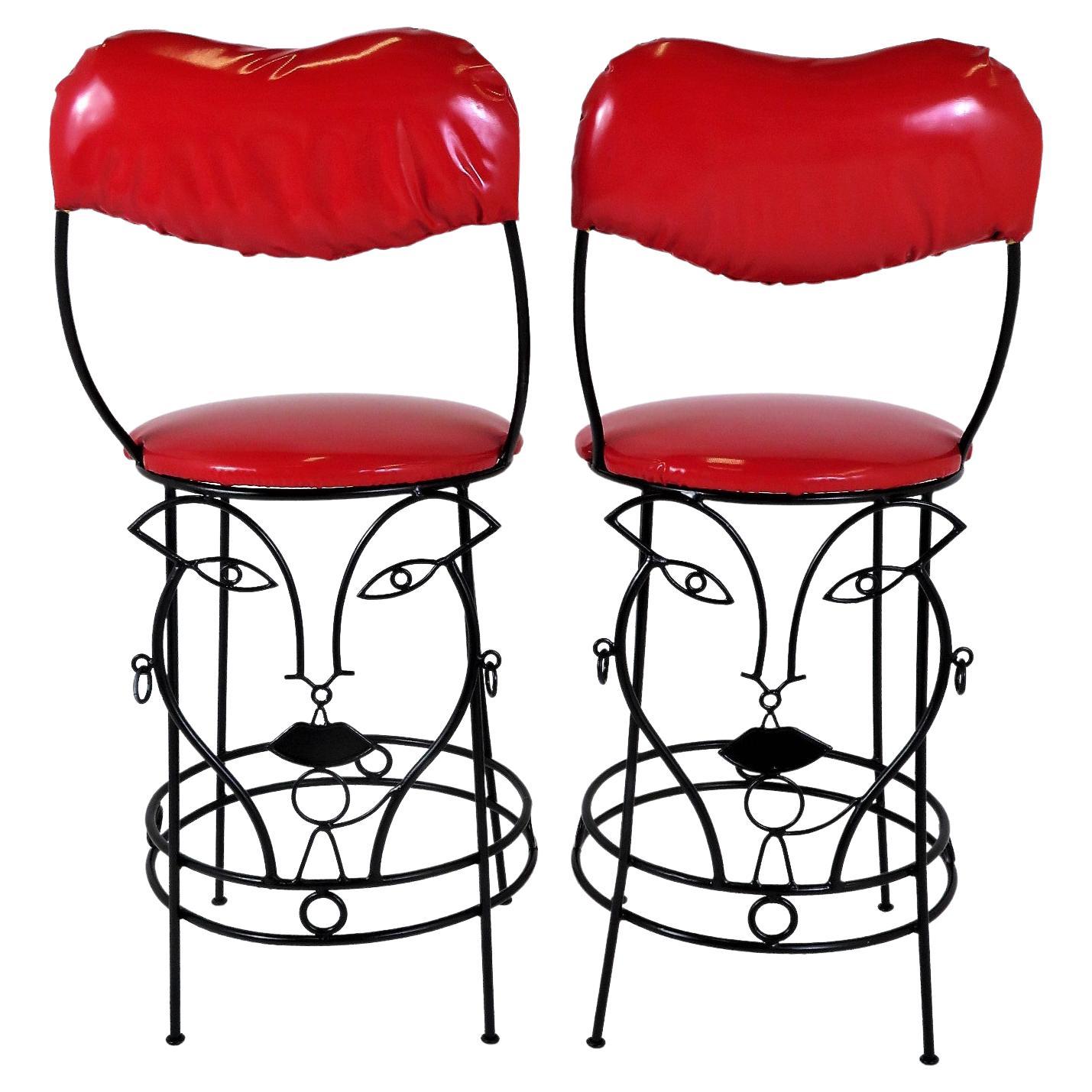 Unique and a delight, this pair of blackened wrought iron Bar Stools have John Risley style faces on their lower half.  The candy apple red vinyl seat and lips inspired back cushion are vintage upholstery in fine order.  The faces are feminine and