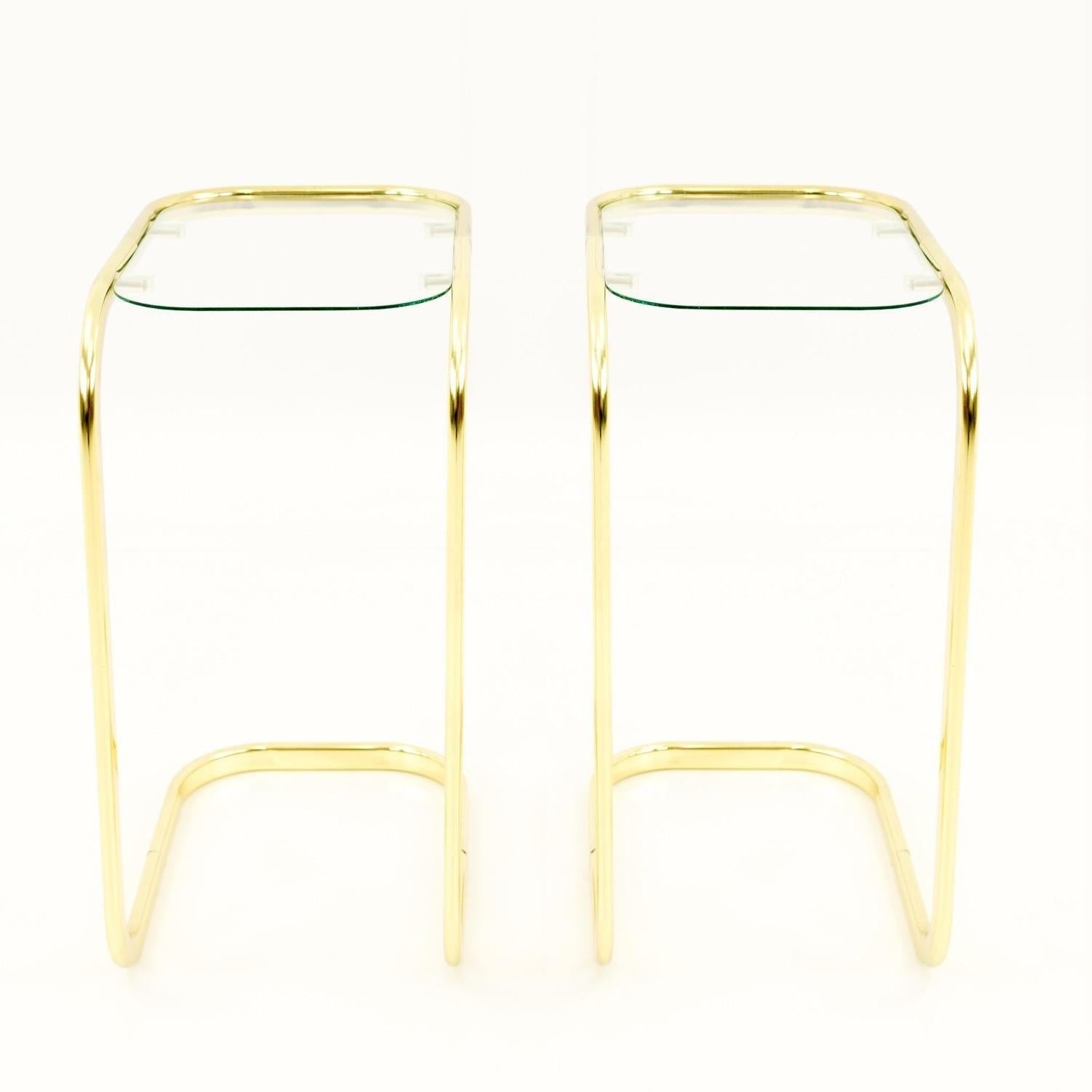 Sleek, stylish pair of brass cantilever occasional / side tables, circa 1970s. A tubular brass frame holds a pill shaped piece of glass. Glass is removable and fits on four rubber suction cups. Perfect for cocktails and hors d'oeuvres.