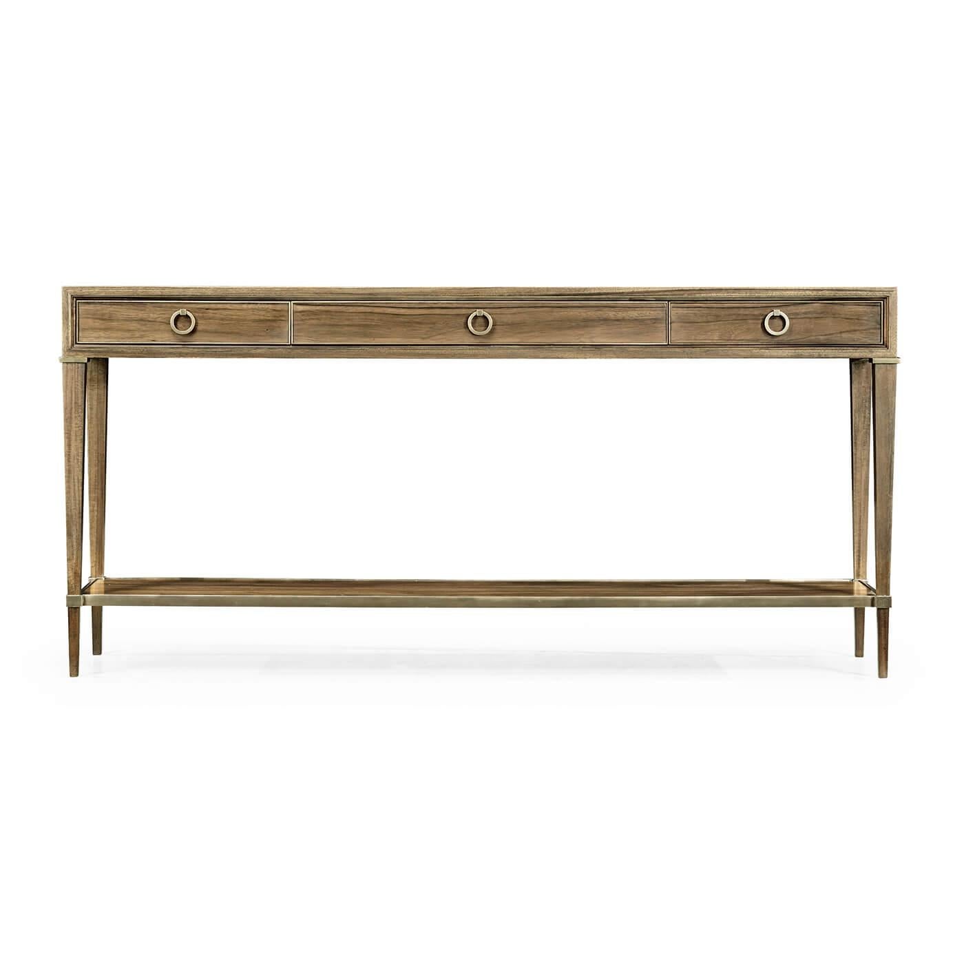 A Regency inspired modern console table with exotic Paldoa wood veneers, with three drawers, brass ring handles, square tapered legs, and a long shelf stretcher base. 

Dimensions: 70