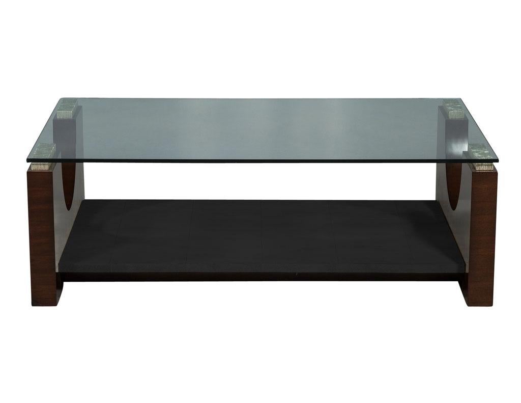This modern deco style cocktail table is crafted out of wood and parchment, this piece has a large glass top and two U-shaped lacquered wood ends with metallic wood pieces for supporting the glass. There is also a large lower shelf with a