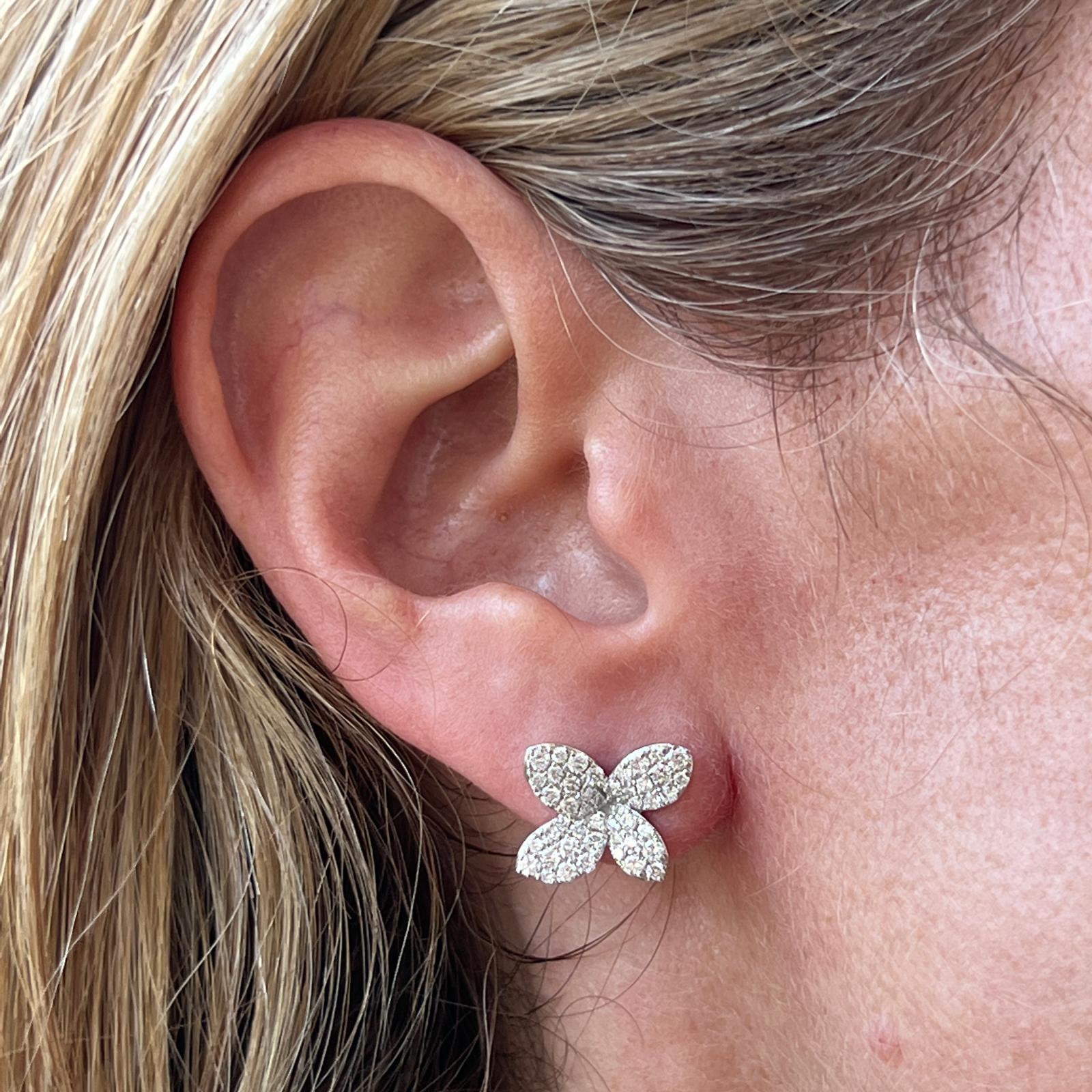 Diamond floral stud earrings fashioned in 18 karat white gold. The flowers feature pavé set diamonds weighing 1.00 carat total weight and graded G-H color and SI clarity. The earrings measures 16 x 16mm,  butterfly backs. 
