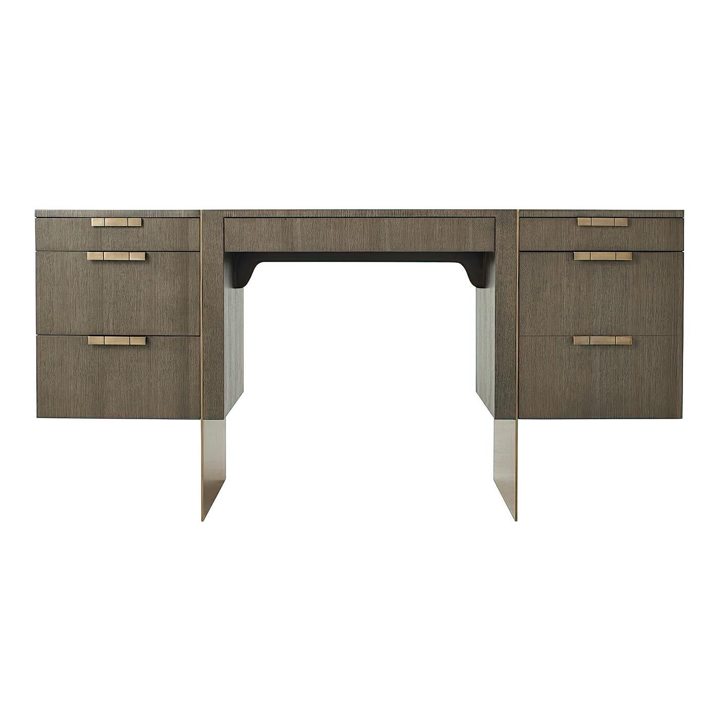 A modern pedestal desk with quartered oak veneer and with a basalt finish. With brass slab legs and handles having a long center drawer and three graduated drawers to your left, and one drawer above a filing drawer to your right. Also with self