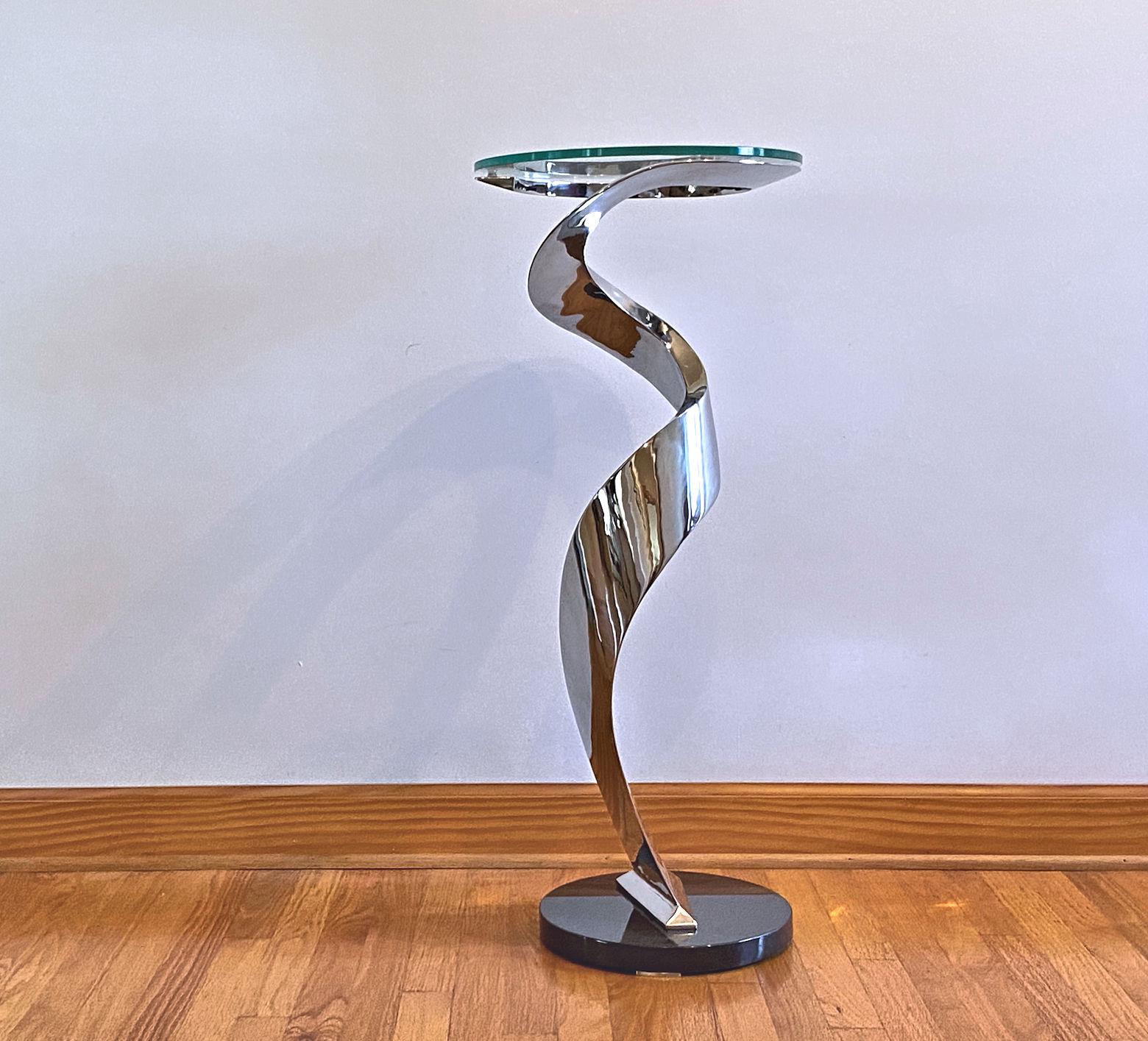 This is not only a table but a piece of sculpture as well. The table is an isosceles triangle in cross section and is like a ribbon of steel winding around so that it appears to be in motion. 
The top is 3/8