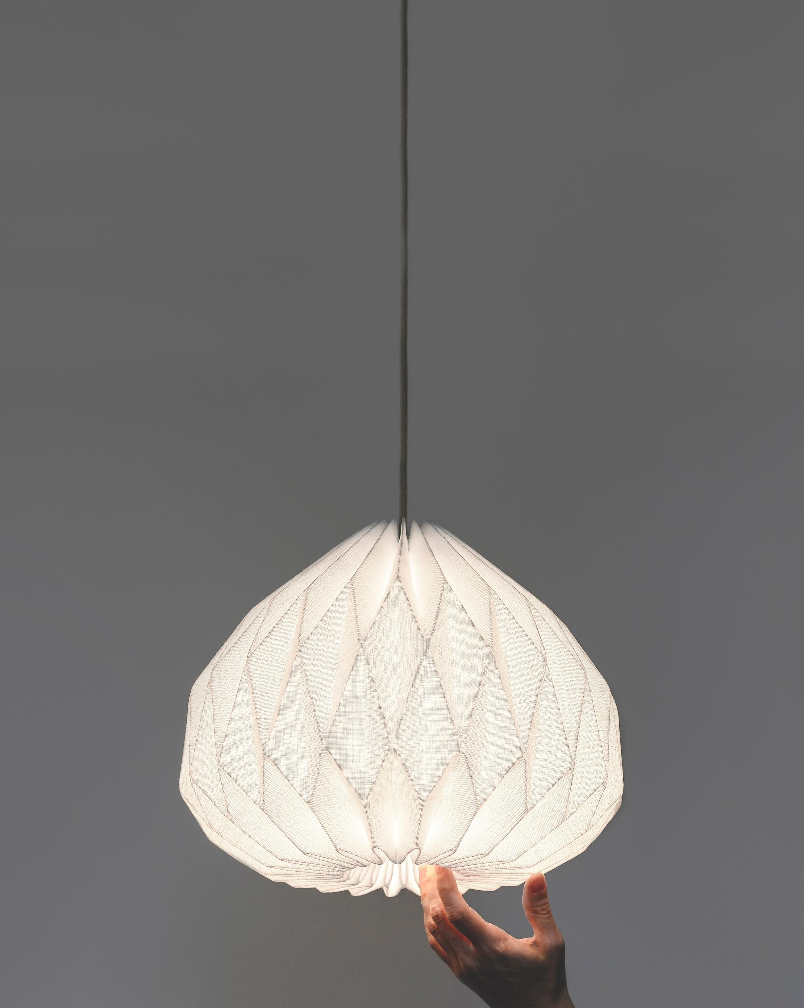 Cette lampe suspendue de style moderne ajoutera une œuvre d'art intéressante et fonctionnelle à votre intérieur.
Fabriqué en tissu de ligne laminé plié à la main, l'abat-jour suspendu fournit un éclairage d'ambiance doux tout en conservant une