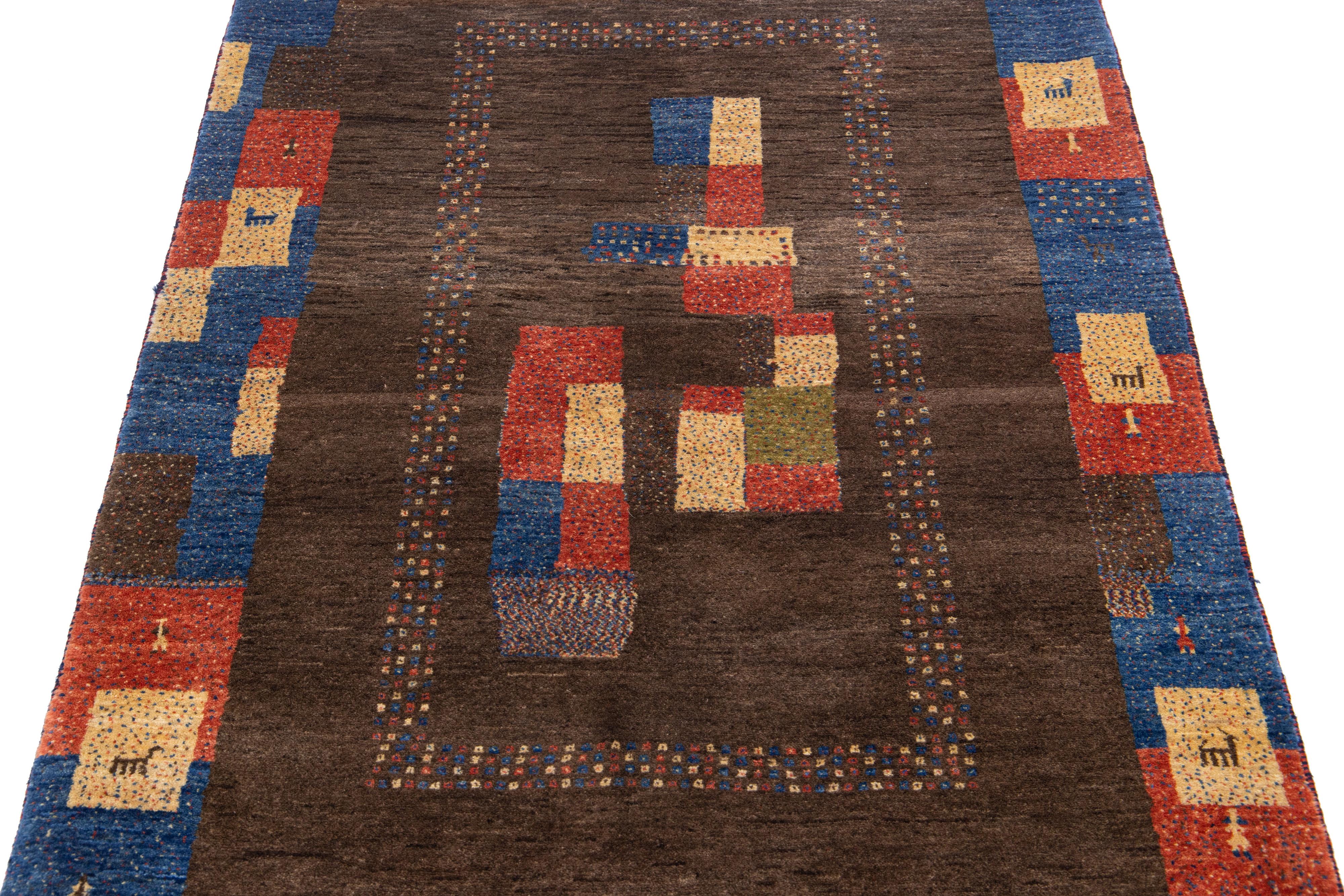 Magnifique tapis moderne en laine tissée à la main de style Gabbeh, avec un champ de couleur marron. Ce tapis persan présente un superbe design minimaliste avec un cadre bleu marine et des accents multicolores.

Ce tapis mesure : 3'6