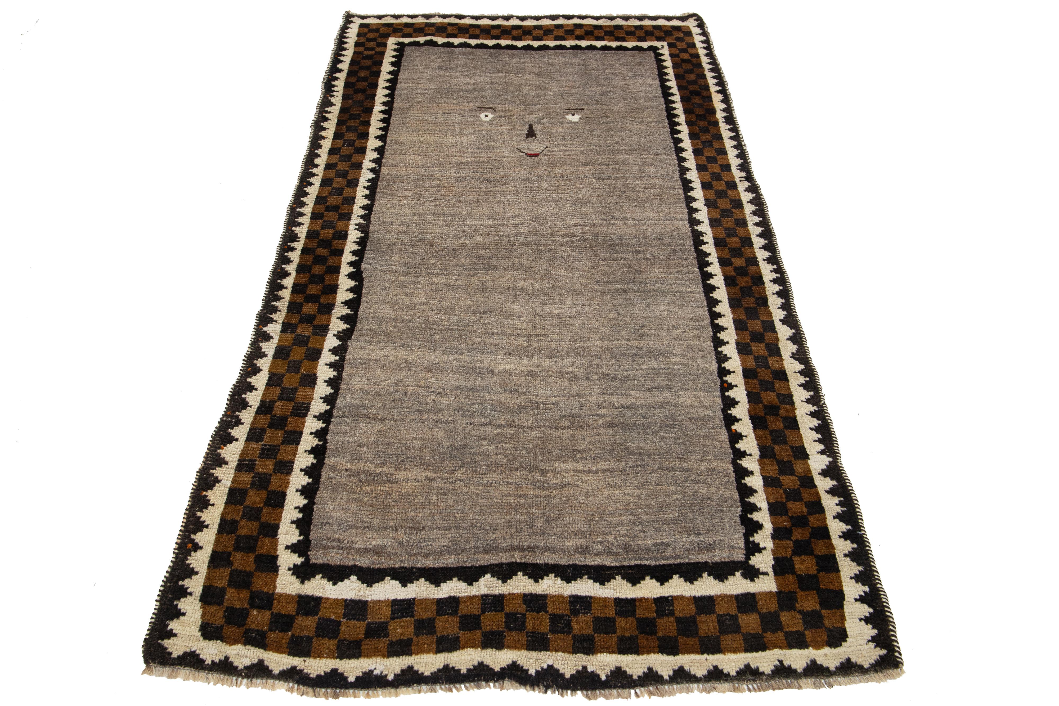 Dieser moderne Gabbeh-Teppich zeichnet sich durch ein handgeknüpftes Design mit modernen geometrischen Mustern aus. Der hellbraune und graue Sockel wird durch beigefarbene, goldbraune und schwarze, rahmengemusterte Details ergänzt.

Dieser Teppich