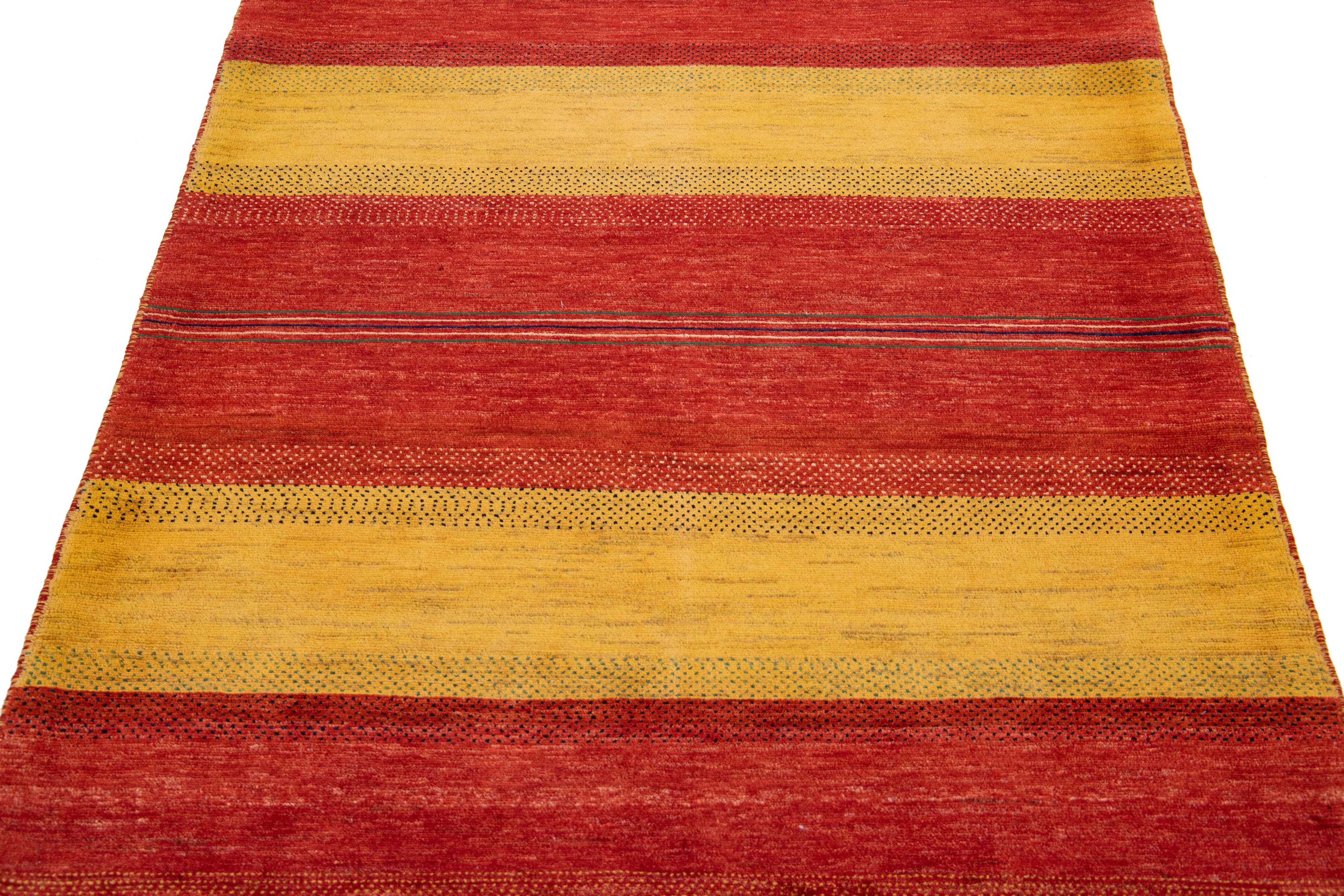Schöner, moderner, handgewebter Wollteppich im Gabbeh-Stil mit einem roten Farbfeld. Dieser Perserteppich hat ein wunderschönes minimalistisches Design mit blauen und gelben Akzenten.

Dieser Teppich misst: 3'11