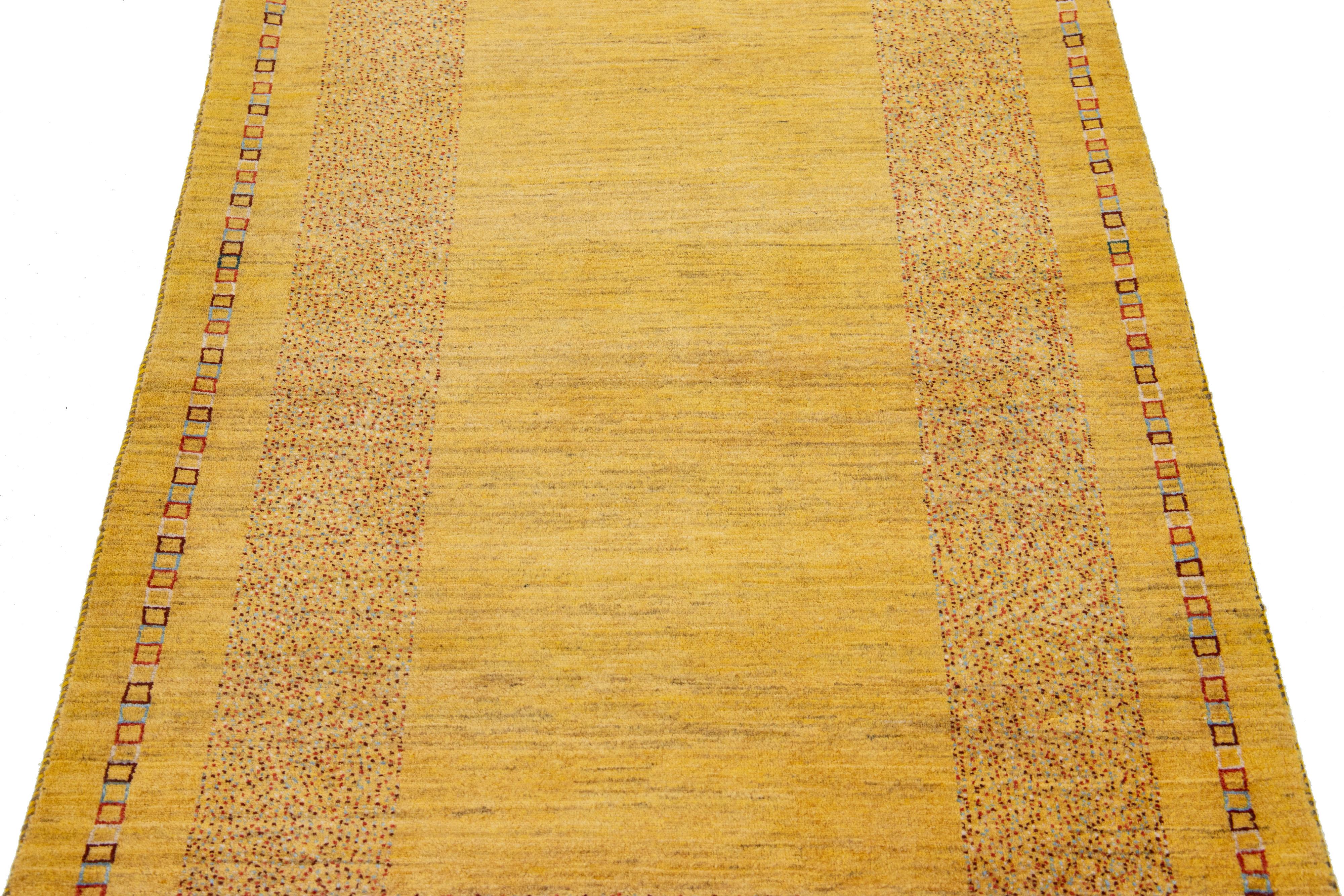 Magnifique tapis moderne en laine tissée à la main de style Gabbeh avec un champ de couleur jaune. Ce tapis persan présente un superbe design minimaliste avec des accents marron, blancs et bleus.

Ce tapis mesure : 3'3