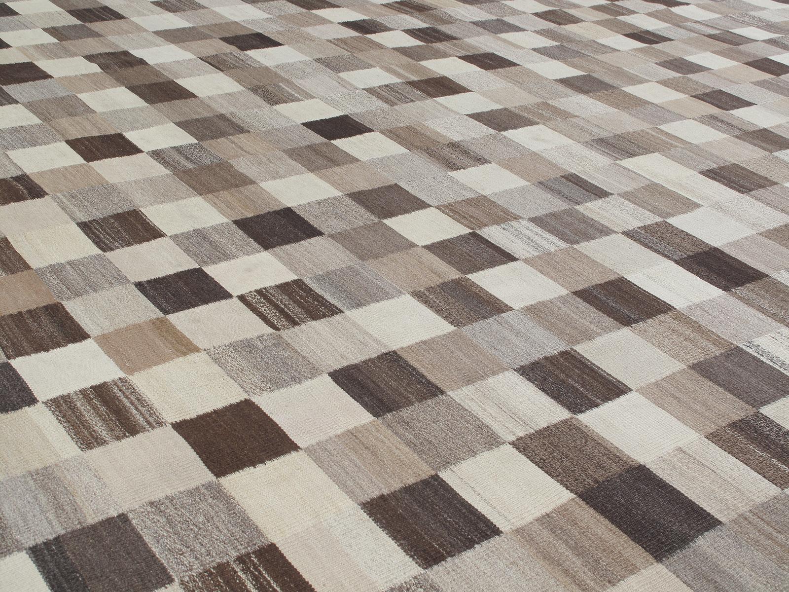 This modern flat-weave rug is made with 100% handspun, non-dyed Persian wool. It features a checkered pattern all made of undyed wool ranging from beige, browns, taupes, and greys. It is inspired by the vintage kilims that are native to the Shiraz