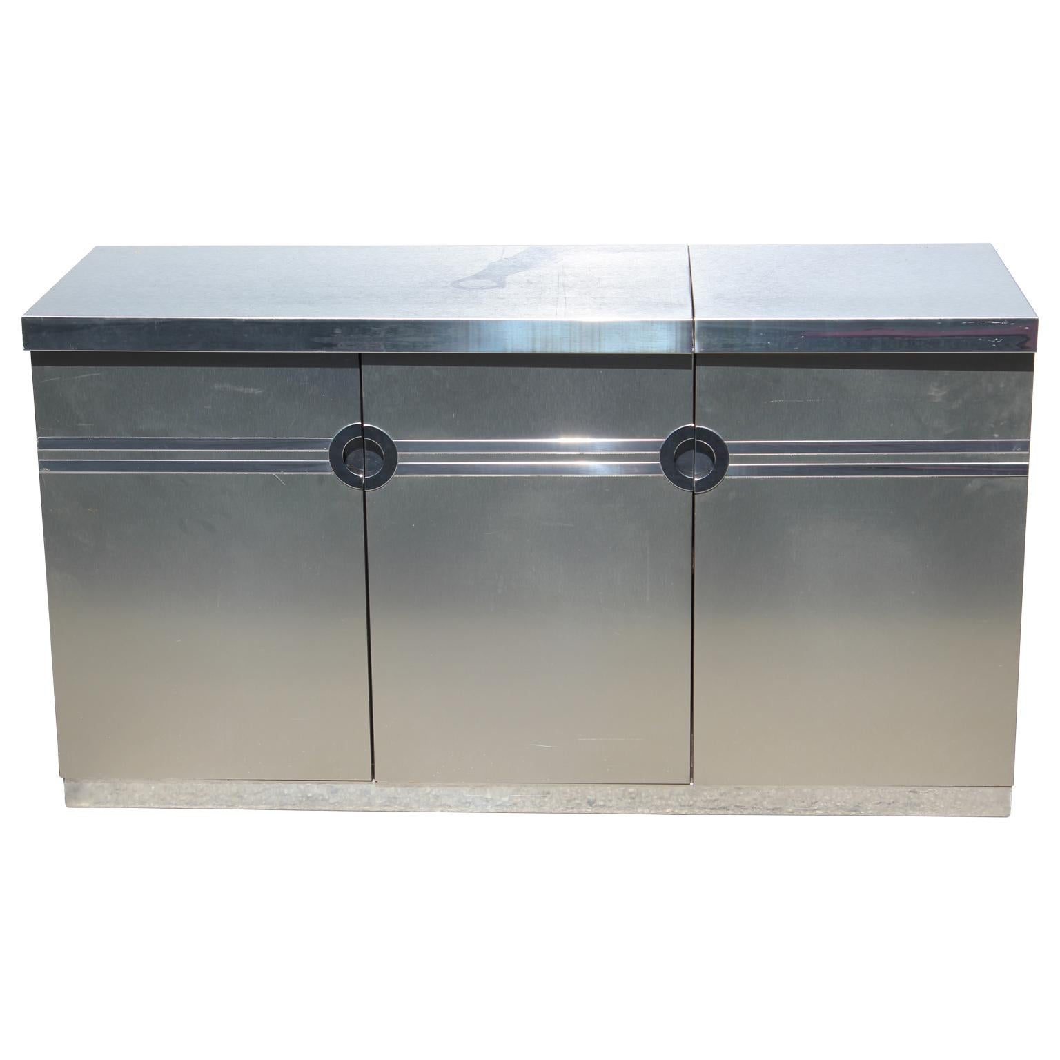 Gorgeous and sleek dry bar by Pierre Cardin made from brushed aluminium and outfitted with a chrome top that flips up to reveal an ice bucket and a place to store glasses with a mirrored lining.