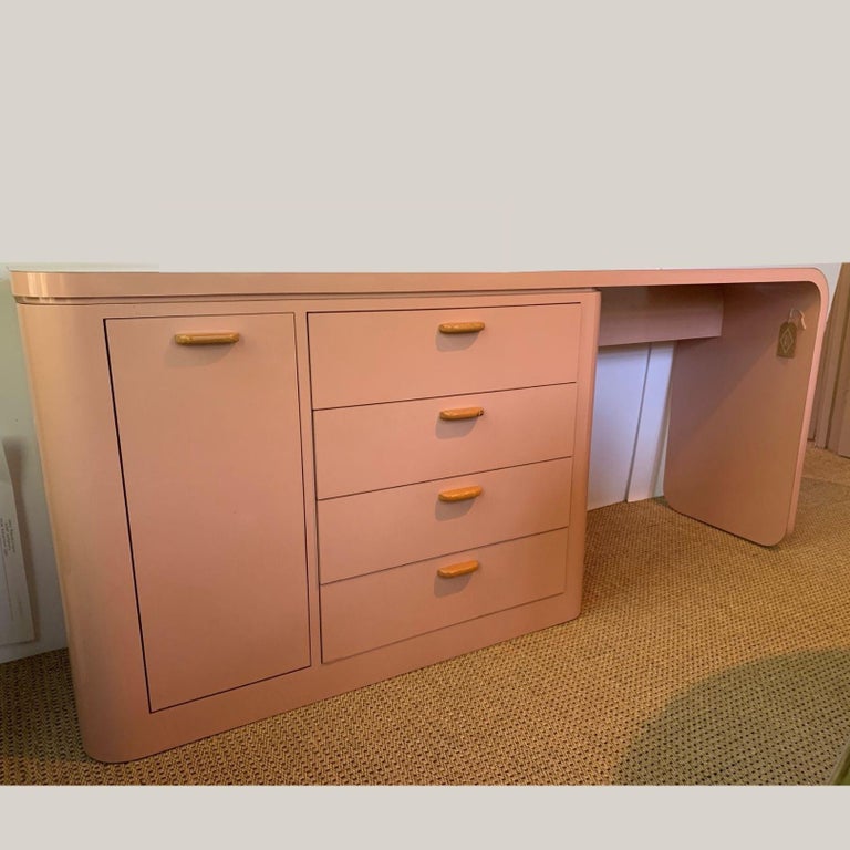 Slim desk or table, modern style, pink laminate with storage cabinet and drawers on the left side. Cabinet has two clear acrylic organizers that slide out and one clear acrylic shelf (non-adjustable). Drawers measure 22.25