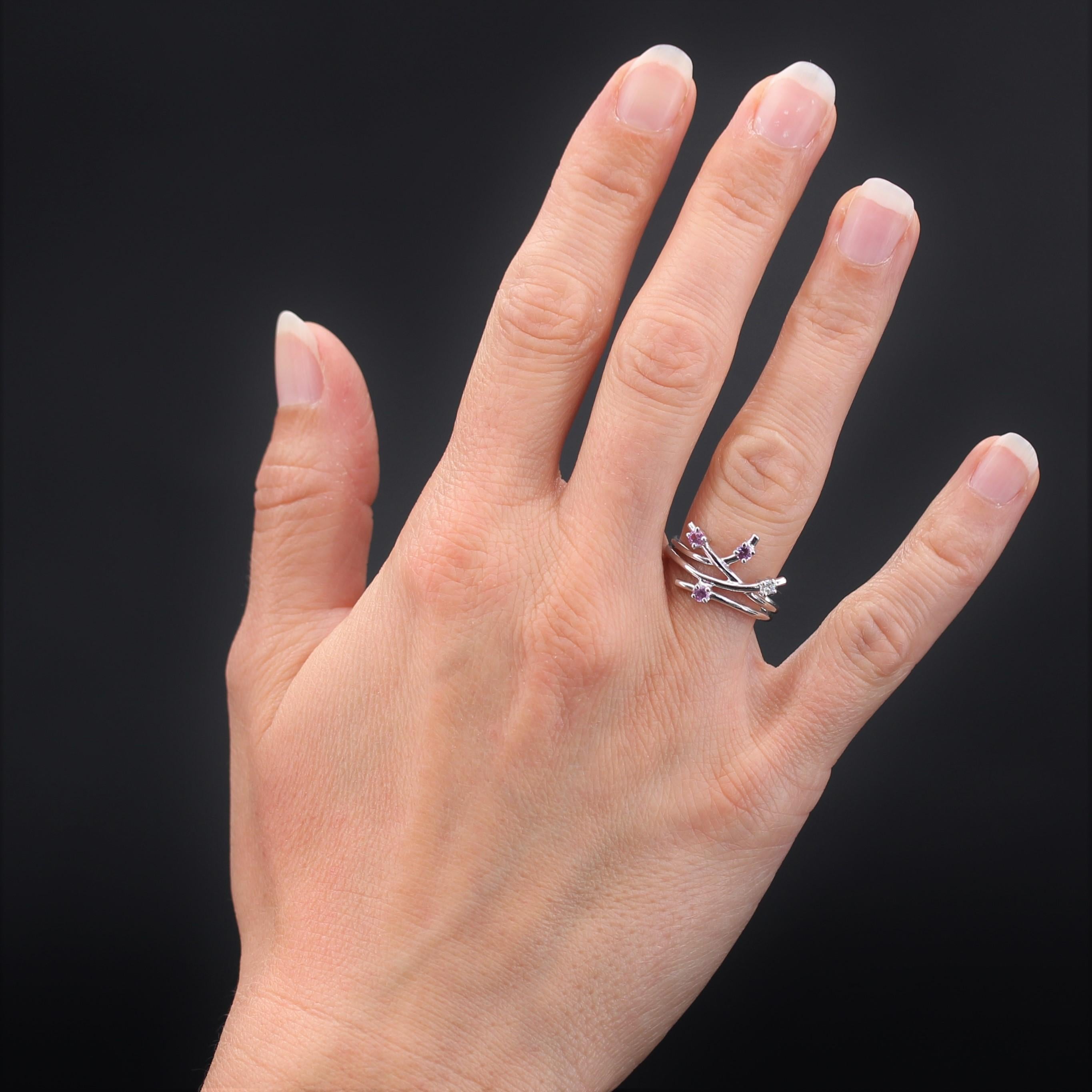 Ring aus 18 Karat Weißgold, Adlerkopfpunze.
Dieser Ring besteht aus 3 Weißgoldfäden, die sich auf der Vorderseite asymmetrisch trennen, und ist mit 4 Klauen mit 3 rosa Saphiren und einem Diamanten besetzt.
Höhe: 1,3 cm, Breite des Musters: 1,7 cm,