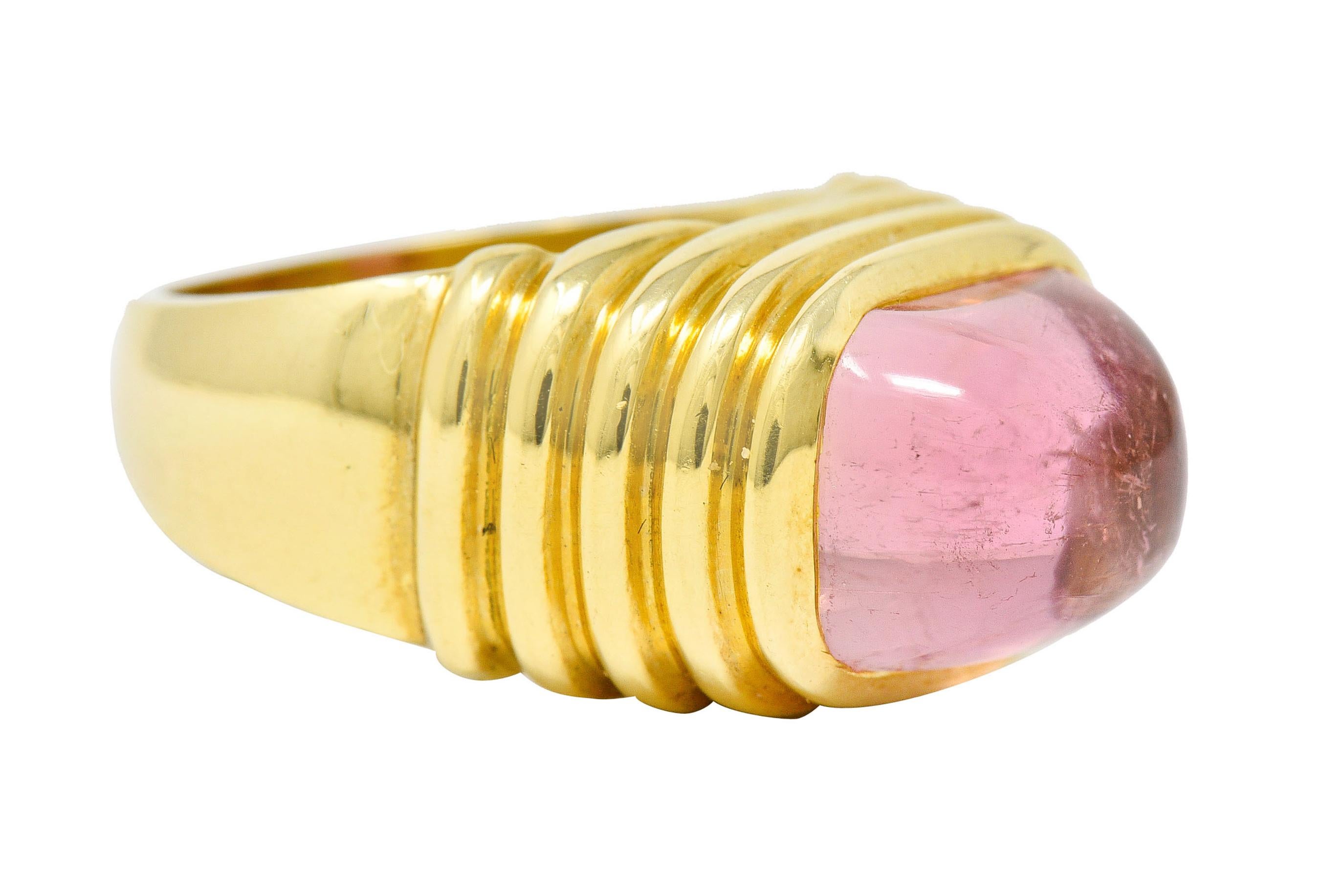 Centering a cushion cut cabochon of tourmaline measuring approximately 11.8 x 8.8 mm

Medium light pink and semi-transparent with natural inclusions

Bezel set in a multi-tiered and ribbed gold surround

Tested as 18 karat gold

Circa: 2000s

Ring