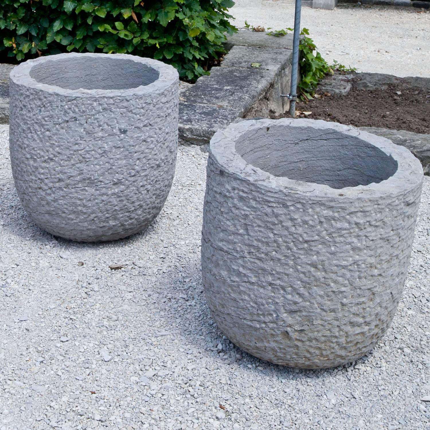 Paar handgeschnitzte, moderne Pflanzgefäße mit runder Grundform, geschwungener Wandung und grob gehämmerter Oberfläche aus Blaustein.