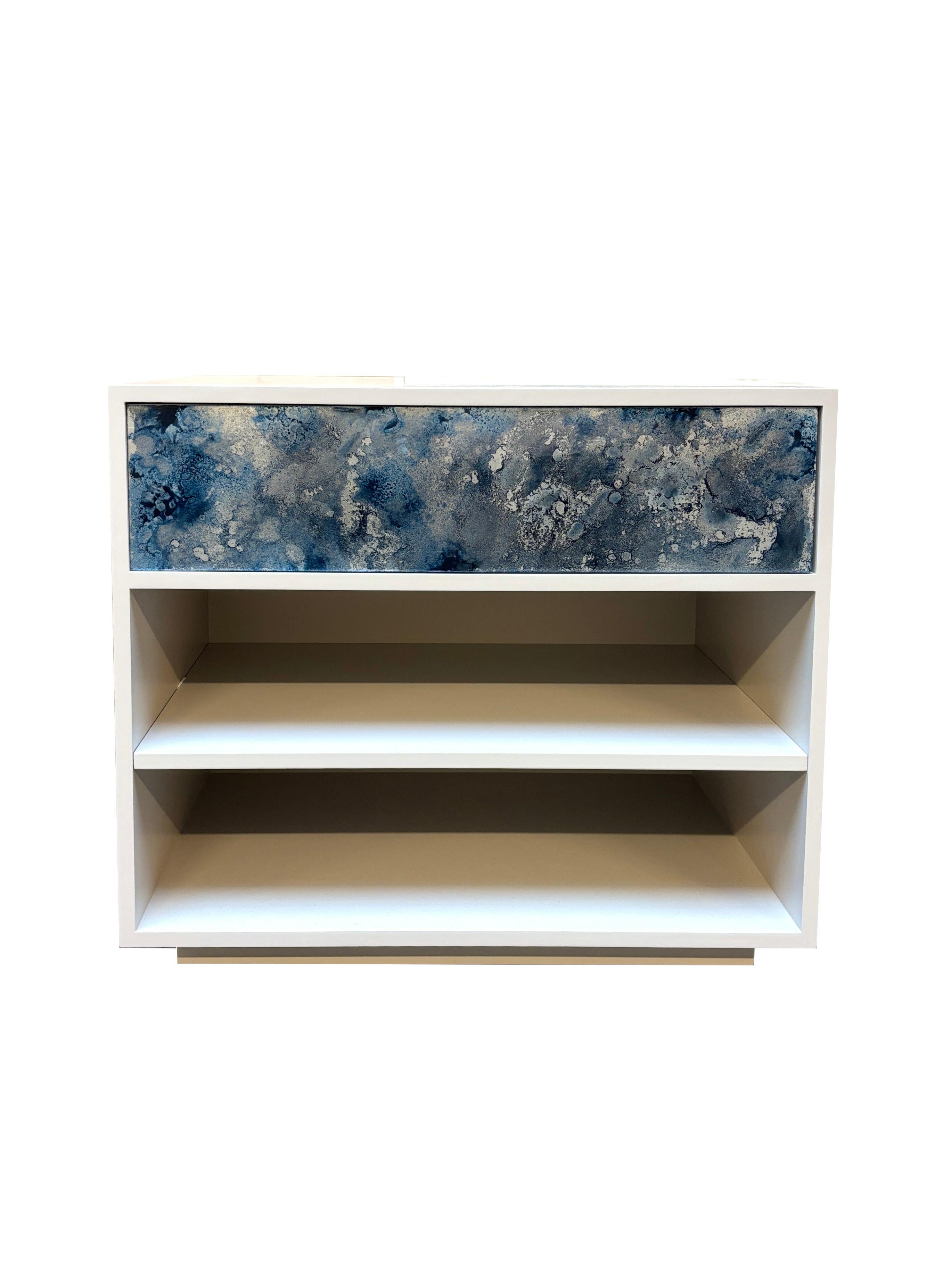 This Modern Platform Ivory One Drawer Nightstand has a single top drawer, and a single shelf in a Light  Lacquer finish The face of the drawer features Midnight Summer hand-painted Mystic Glass, with touch latch. Custom sizes and finishes are