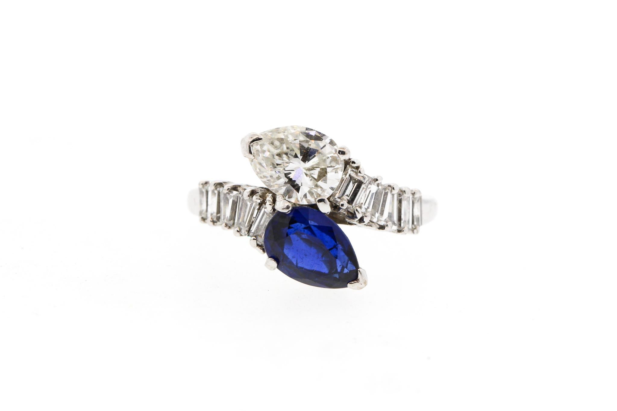 A mid-century platinum sapphire and diamond bypass ring, circa 1960. The ring is set with a white pear shape diamond weighing approximately 1.15 cts and an opposing blue sapphire weighing about the same. The diamond is very clean and white,