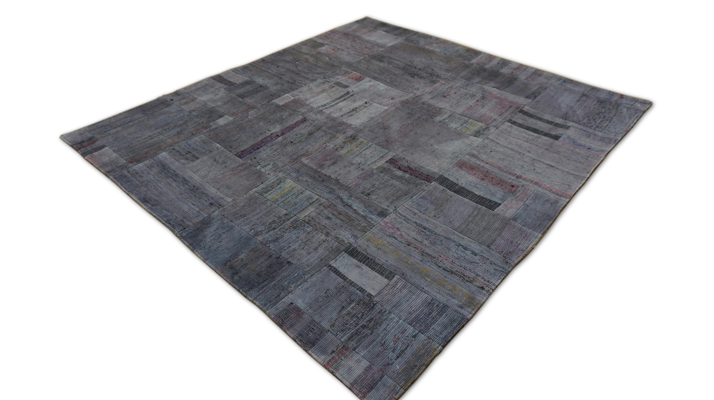 This hand-woven cotton patchwork rug offers a striking example of contemporary design fused with rich vintage soul. Carefully constructed from fragments of repurposed and overdyed in a rich medley of charcoal, gray, and plum tones, this rug boasts a