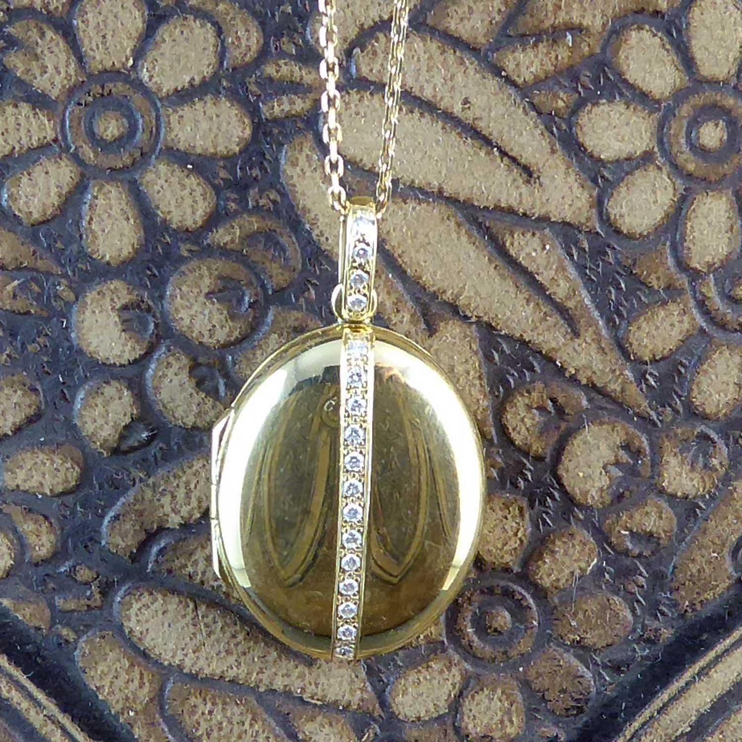 A pre-owned luxury locket crafted in 18ct yellow gold and brilliant cut diamonds by the renowned British locket makers, Charles Green.  The locket is fashioned in a pleasing oval shape of highly polished gold with a central vertical line of 13 pavé