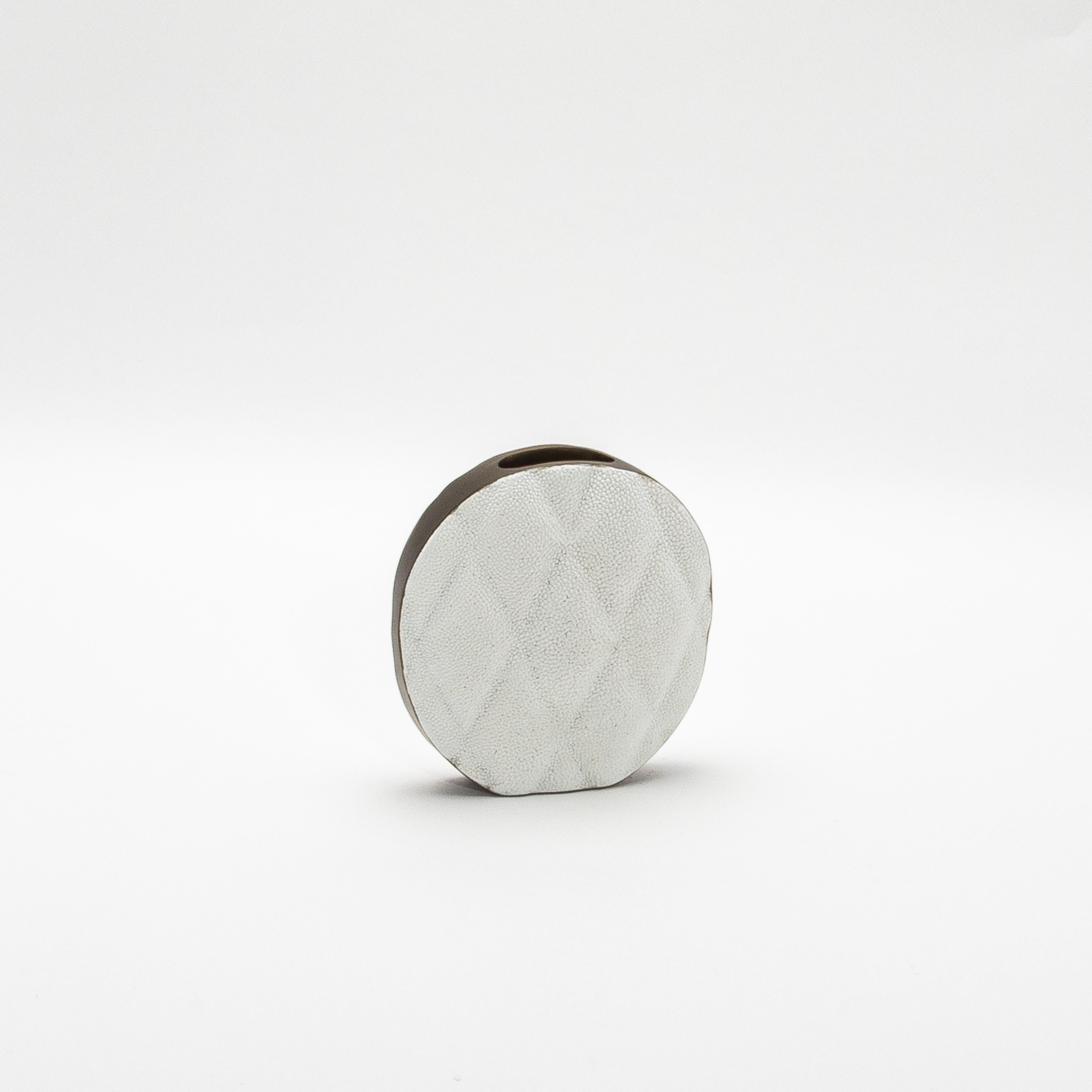 Il vaso Coco di KIFU Paris è un pezzo forte che unisce armoniosamente lusso moderno ed eleganza senza tempo. Realizzato in sontuoso zigrino bianco, la superficie del vaso vanta un sorprendente motivo trapuntato che emana raffinatezza. La texture