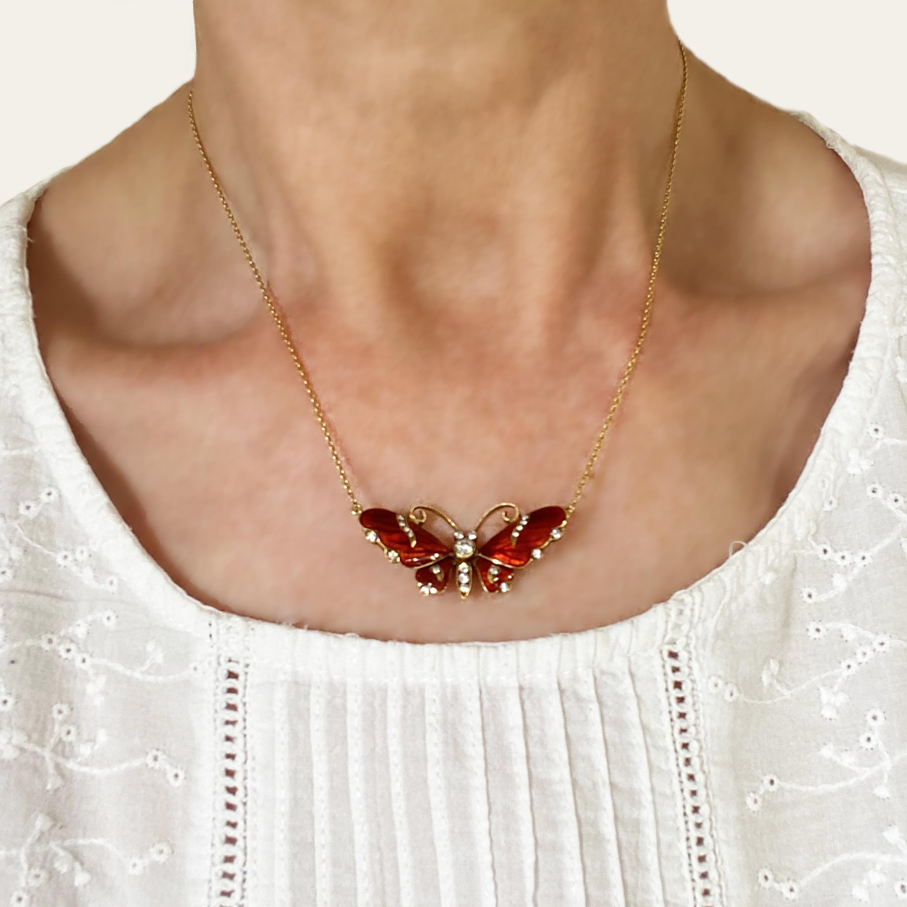 Colgante de mariposa de esmalte rojo, con esmalte guilloché que representa las venas de las alas, con 0,28 ct de diamantes redondos talla brillante, en las alas, los ojos, el tórax y el abdomen, montado en oro, sobre una cadena de oro de traza.