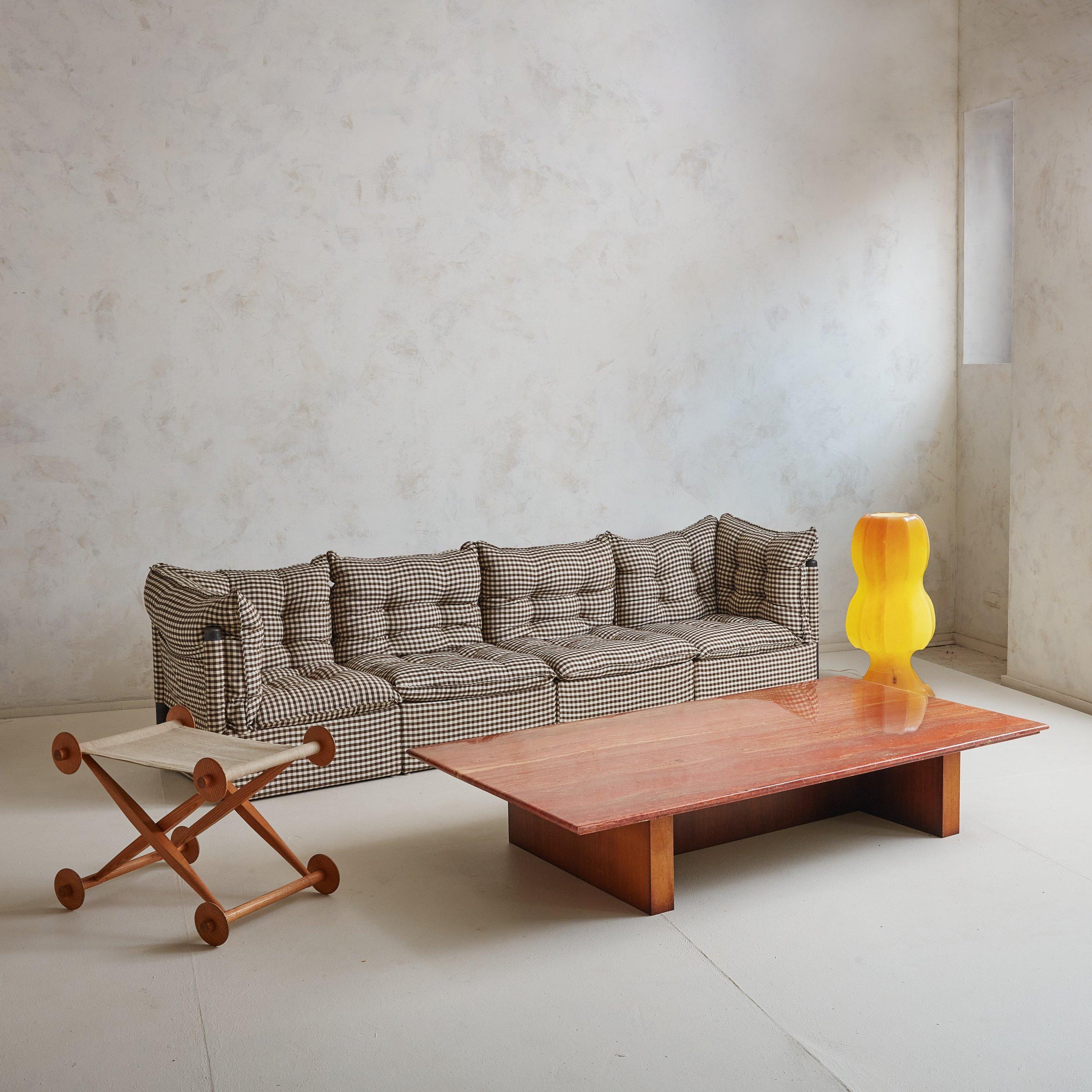 A modern rectangular coffee table constructed of a rare variation of red travertine with a polished finish. Veining is present throughout in hues of orange, coral, and taupe. The travertine top extends over a wooden “H” shaped base, providing