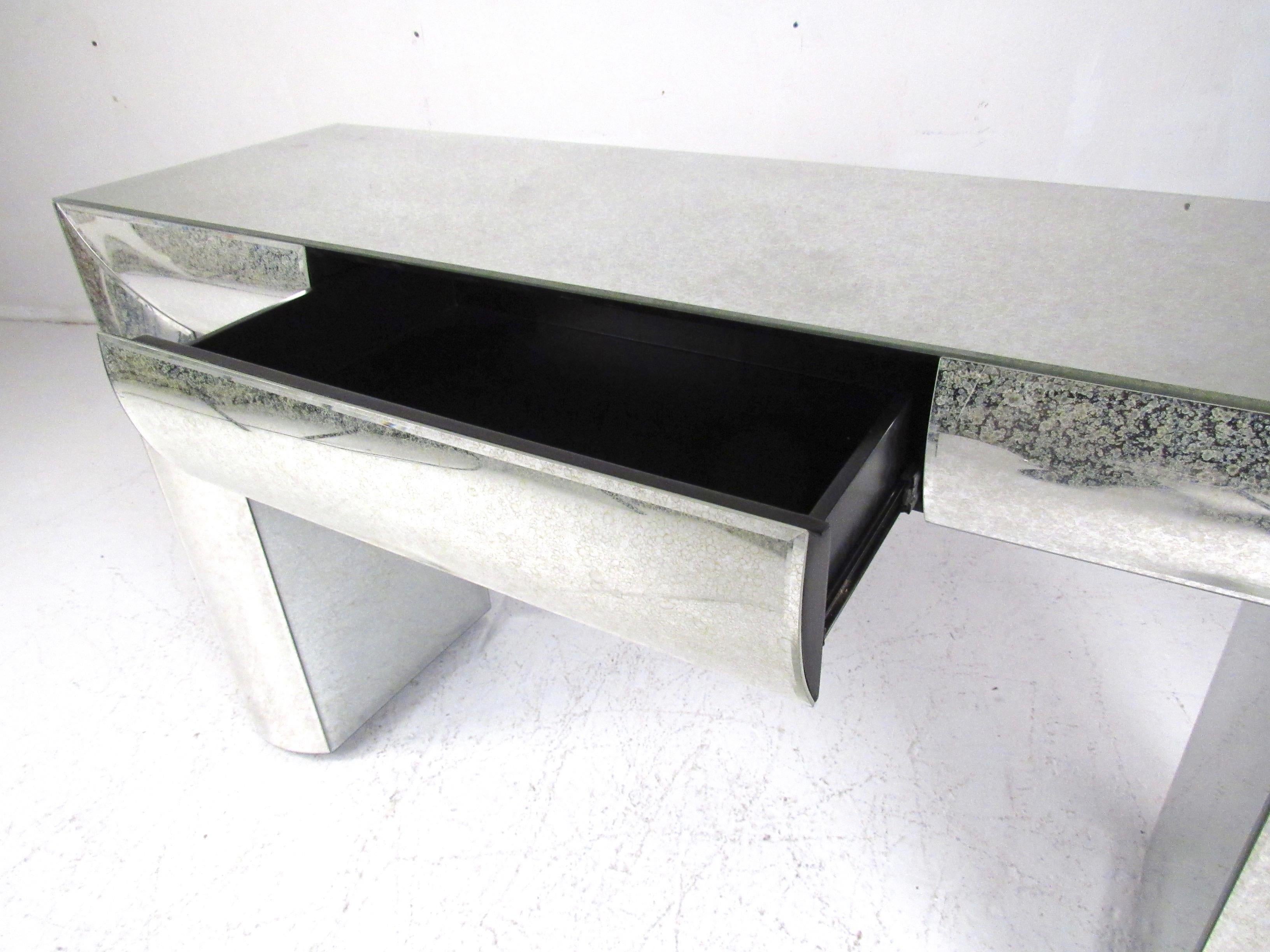 This striking decorator modern console table features antiqued mirror finish with unique rounded sides. Two top drawers allow for added storage should this table be used as a vanity. Impressive Hollywood Regency appeal makes for the perfect addition