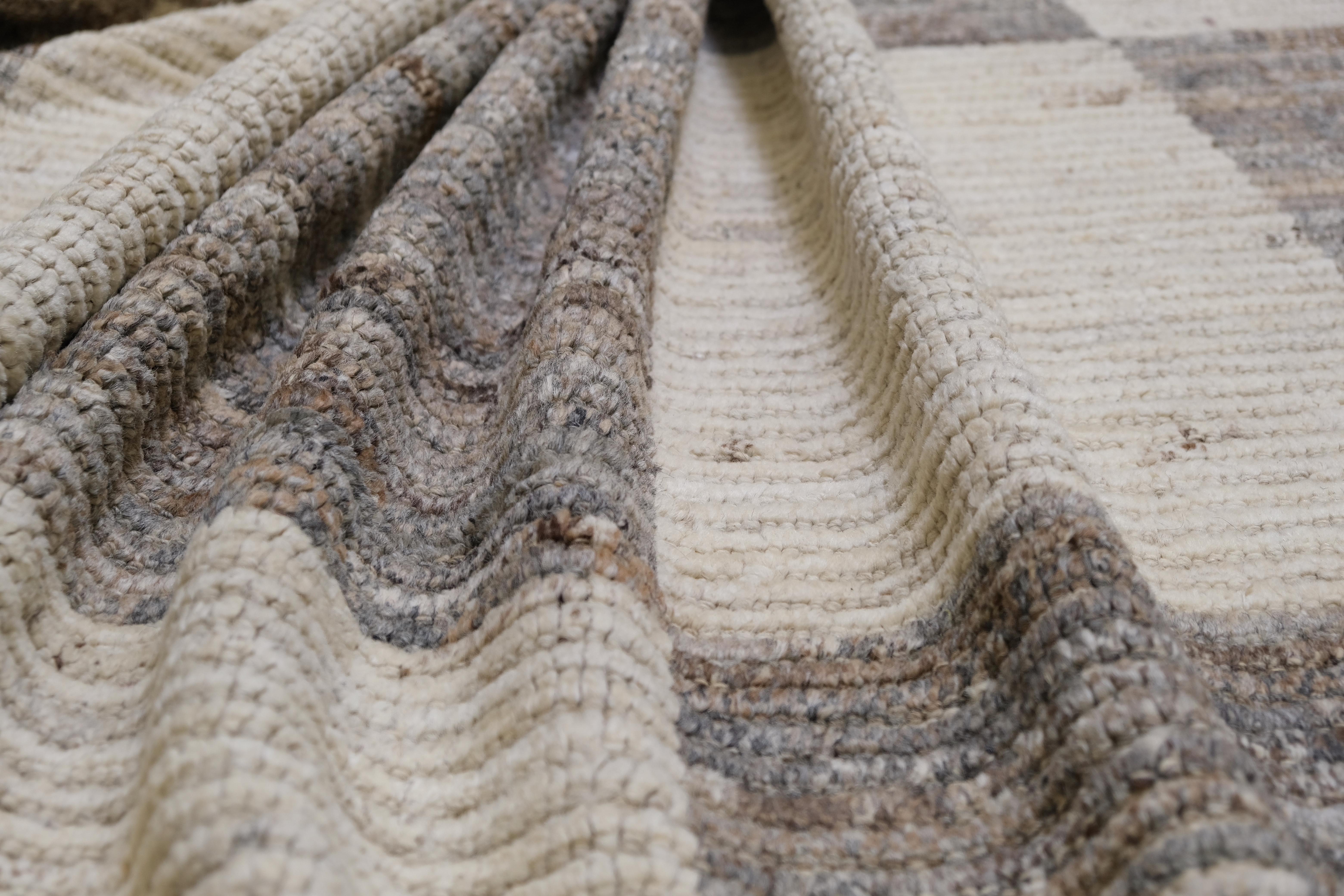 This stunning hand-knotted wool rug, crafted in Afghanistan, showcases a bold and contemporary checkered design. With its intricate linear patterns and a sophisticated mix of neutral earthy tones, this rug is a perfect blend of traditional