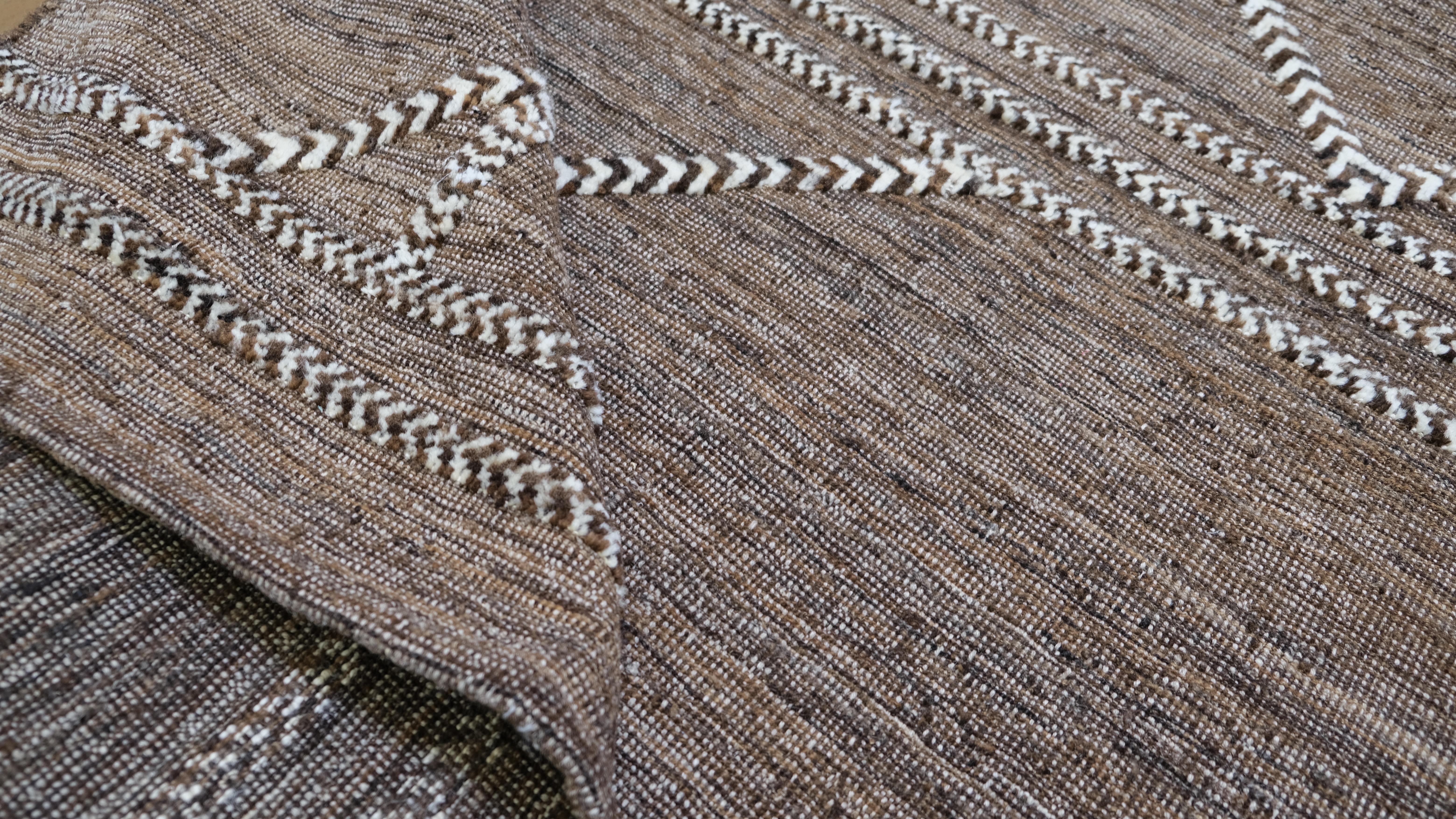 Enhance your living space with this elegant hand-knotted wool rug. Featuring an earthy brown background with intricate white embroidered geometric patterns, this rug combines modern design with artisanal craftsmanship. The minimalist triangular