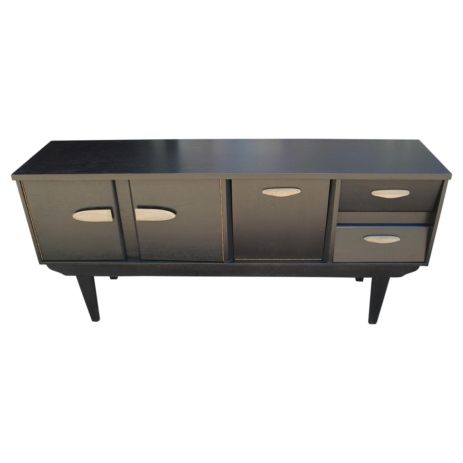 Wonderful modern custom sideboard or credenza newly restored with a black finish and wooden handles. The drawers make a fun accent with angled front panels. This sideboard has two drawers, one middle drop front cabinet, and a larger second cabinet