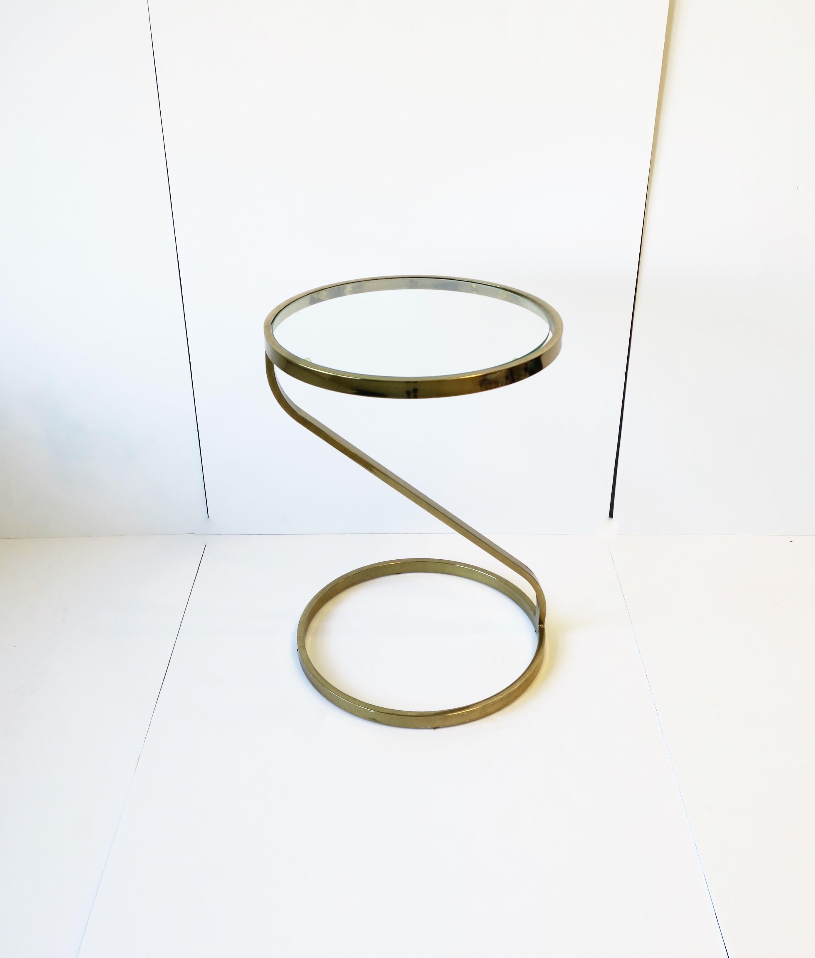 A '70s Modern style round brass-plated and glass side or end table in the style of designer Milo Baughman, circa 1970s, 20th century. Table measures: 17
