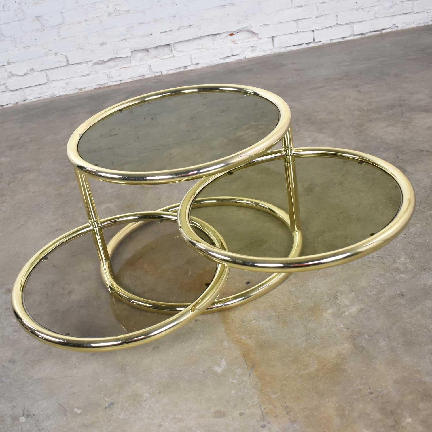 Handsome vintage modern round coffee table, end table, or side table with pivoting tiers in brass tube and smoke glass. It is in wonderful vintage condition. The brass plating has some wear where the steel beneath can be seen but does not detract