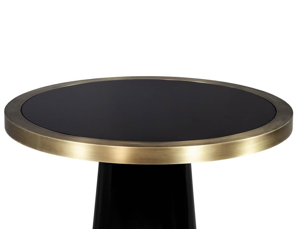 This made to order foyer table is part of the Carrocel Custom collection. The base is crafted out of solid wood with hand polished black lacquer in a slim geometric shape. The tabletop is a black glass inset piece surrounded by a brass ring, adding