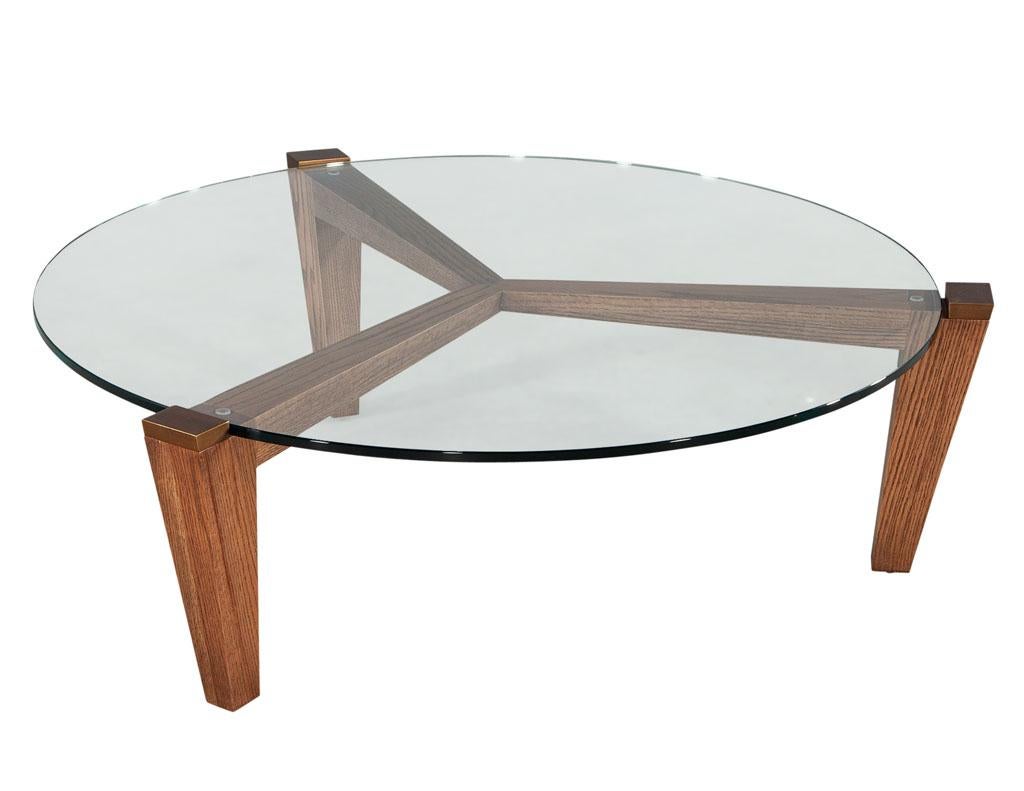 Modern round oak coffee table with metal accents by Ellen Degeneres Salina Table. Sleek mid-century modern inspired glass top coffee table. Featuring unique 3-legged design with antiqued metal accents. Glass top nests between the metal accents
