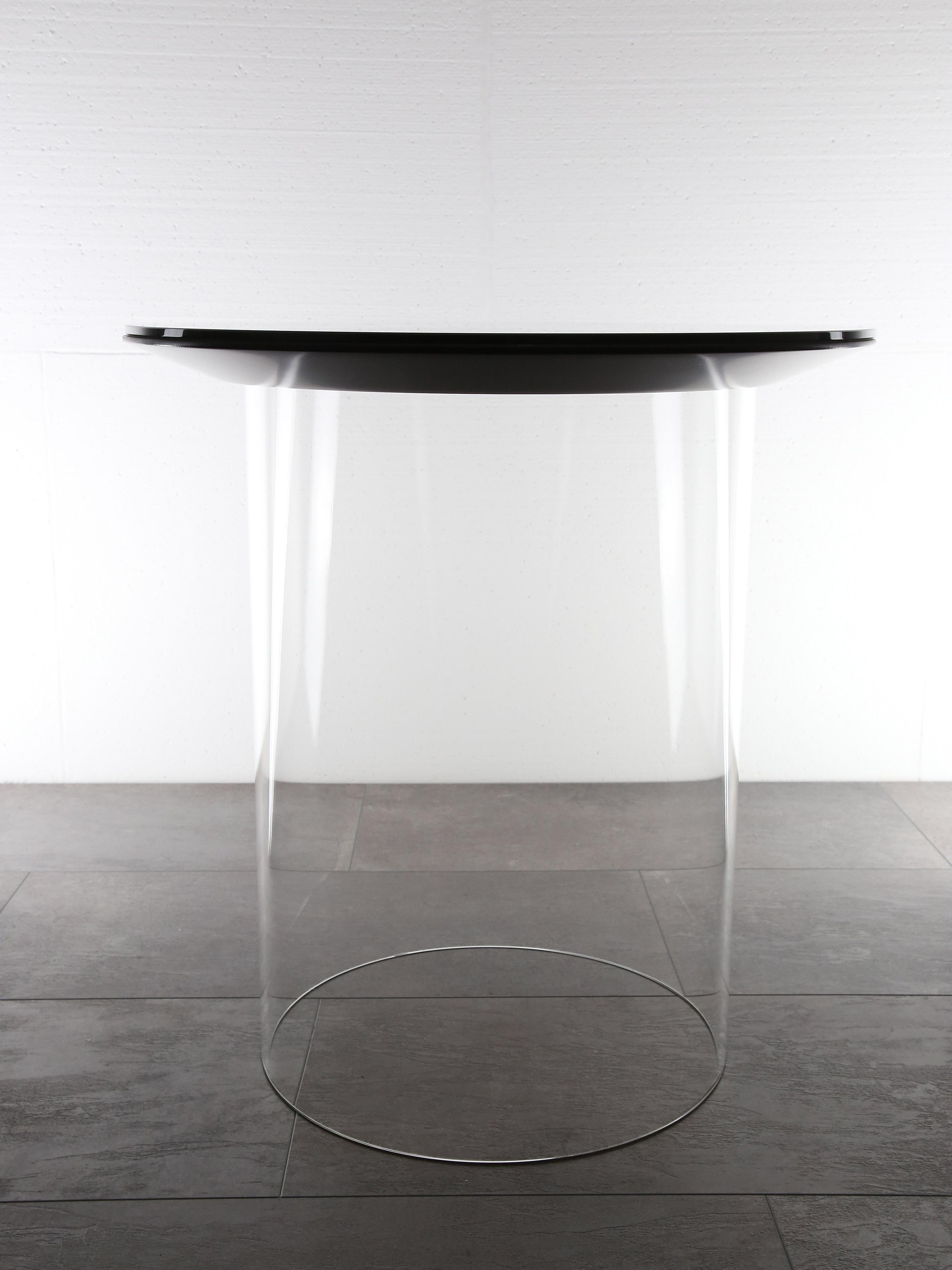 Award-winning side table dontCme is made of borosilicate glass, solid colored glass and lacquered MDF. 

The main topic of this work was to disguise the static necessities of furniture. As a result, carried by a glass cylinder, the round frame