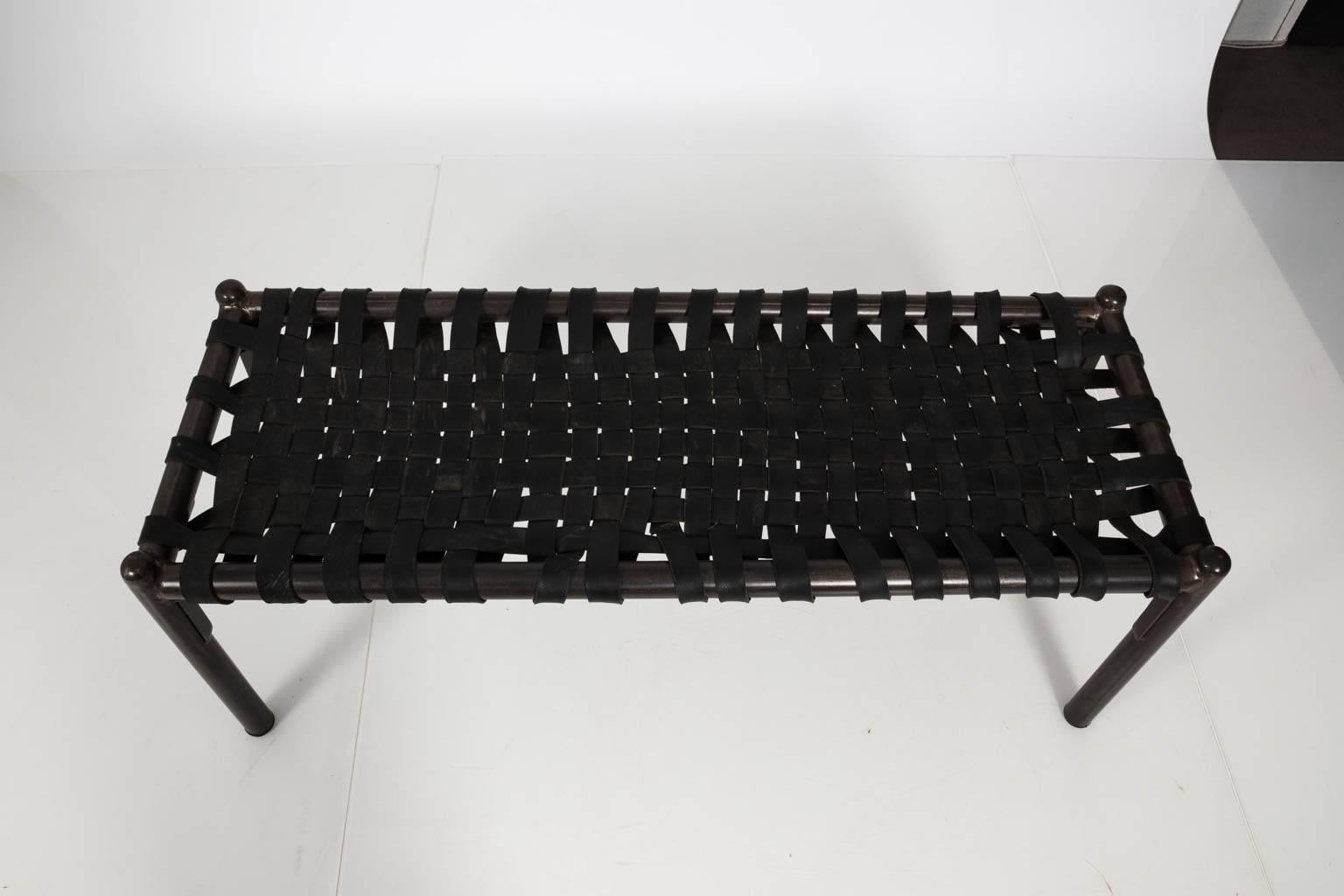 Mid-Century Modern style woven rubber strap bench with a black metal frame on teak wood legs.
 
