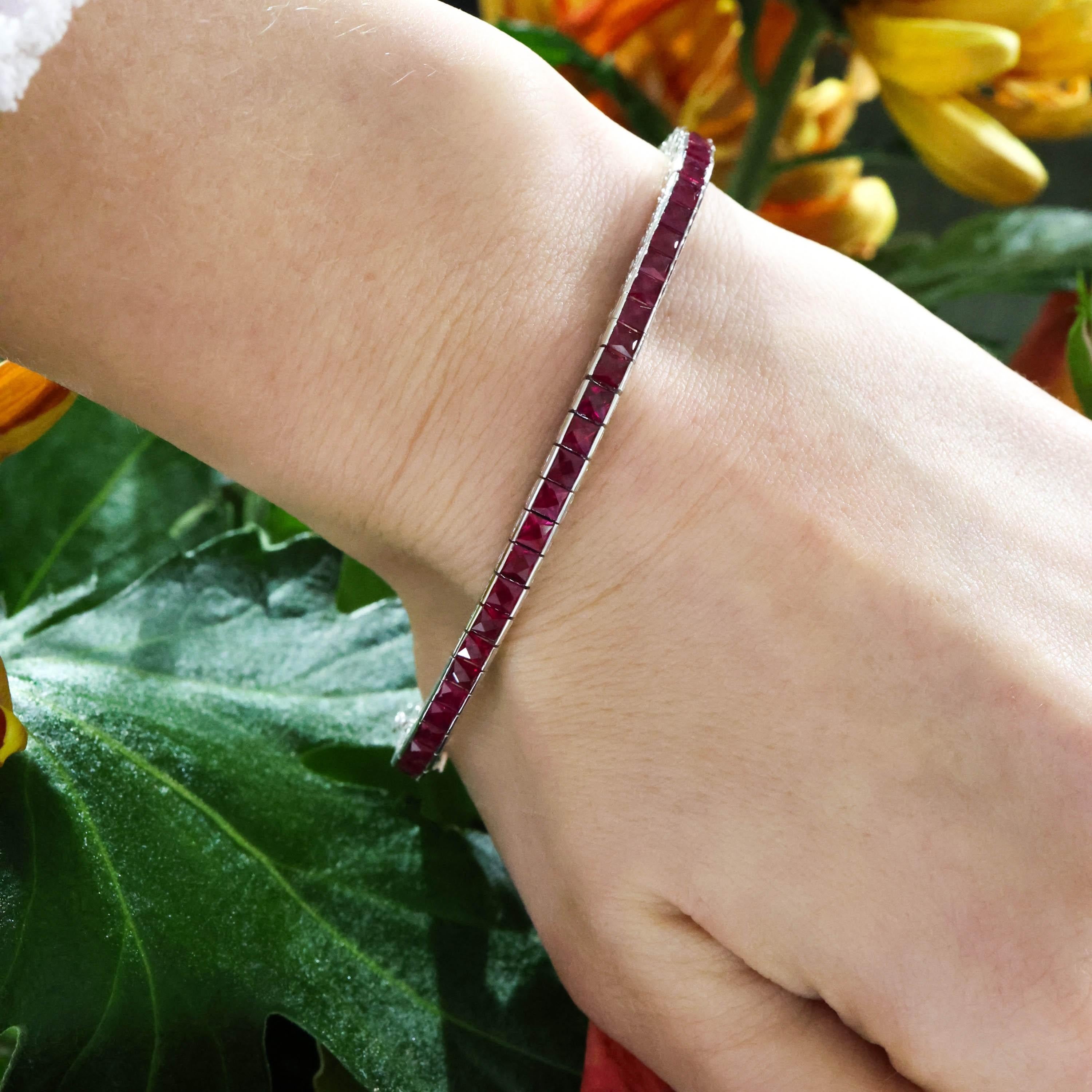 A modern ruby and platinum line bracelet, channel set with a single row of French-cut rubies, in individually hinged links, with foliate engraved, openwork sides, with a box and tongue clasp, with a safety catch, mounted in 900 standard platinum.