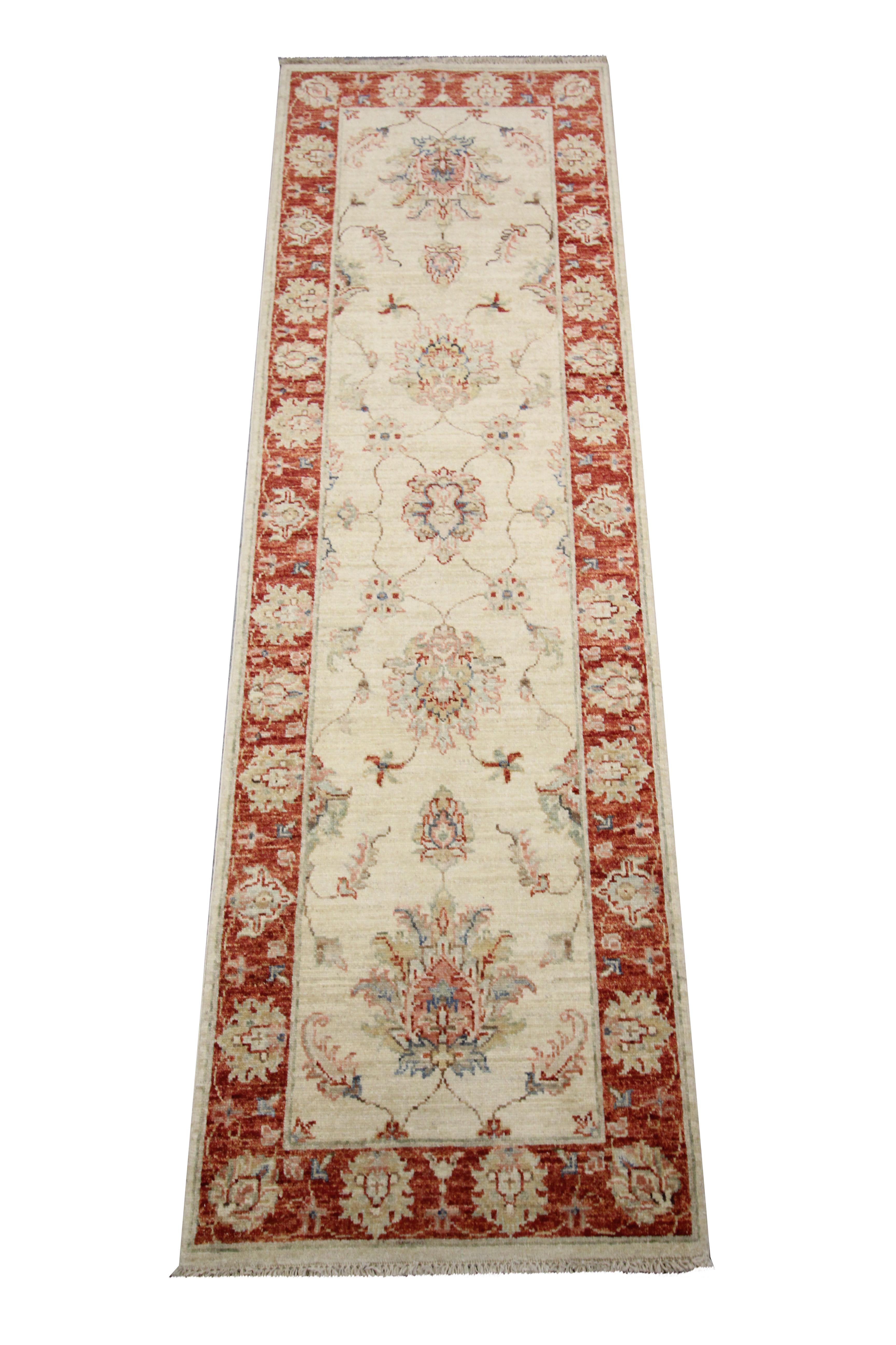 This elegant wool runner rug is a handwoven vintage carpet constructed by hand with a traditional Ziegler design. The central design has been woven on a simple cream background with a long-established traditional floral design woven in red and beige