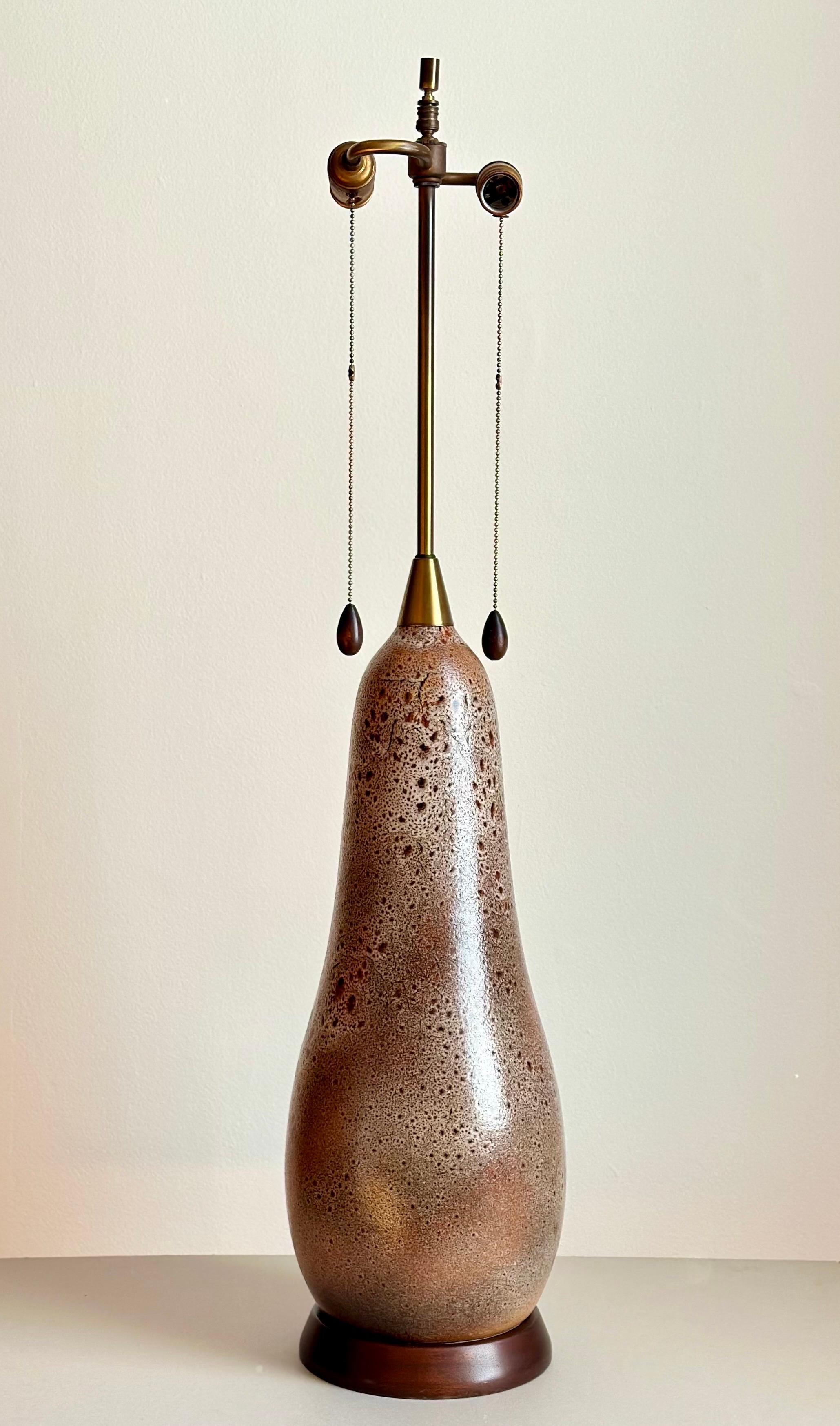 Large scale mid-century modern ceramic table lamp comprising a pear-shaped ceramic body finished with a salt glaze in muted earth tones, supported by a walnut base and with matching walnut switch pulls. A high quality lamp with its original