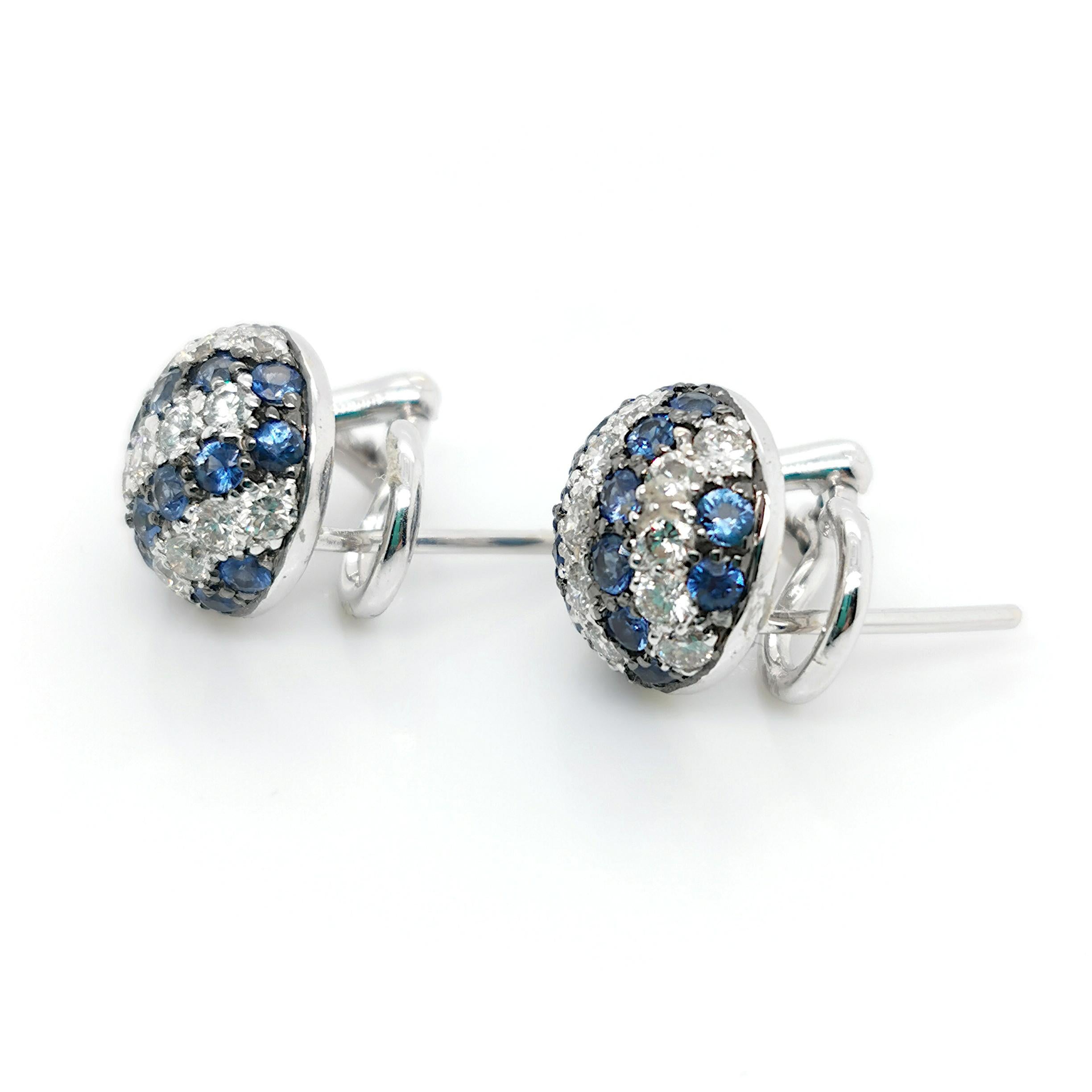 A pair of sapphire and diamond earrings, with a circular dome, set with alternating rows of round brilliant-cut diamonds and round faceted sapphires, mounted in 18ct white gold, with post and clip fittings. Estimated total diamond weight 1.00ct.