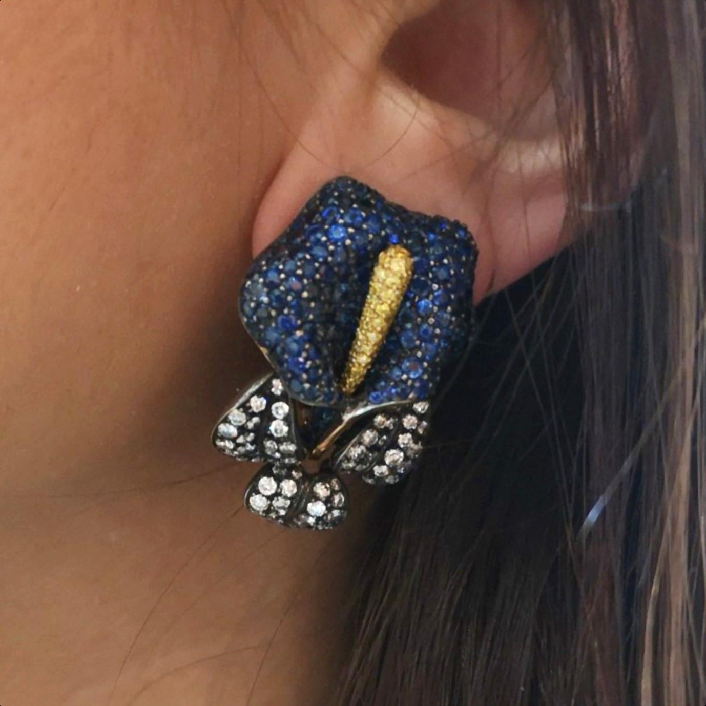 A pair of modern, Moira design, calla lily flower earrings, with pavé set sapphire spathes, yellow diamond set spadices and round brilliant-cut diamond set leaves, mounted in gold with silver settings, with collapsible posts and clip fittings,