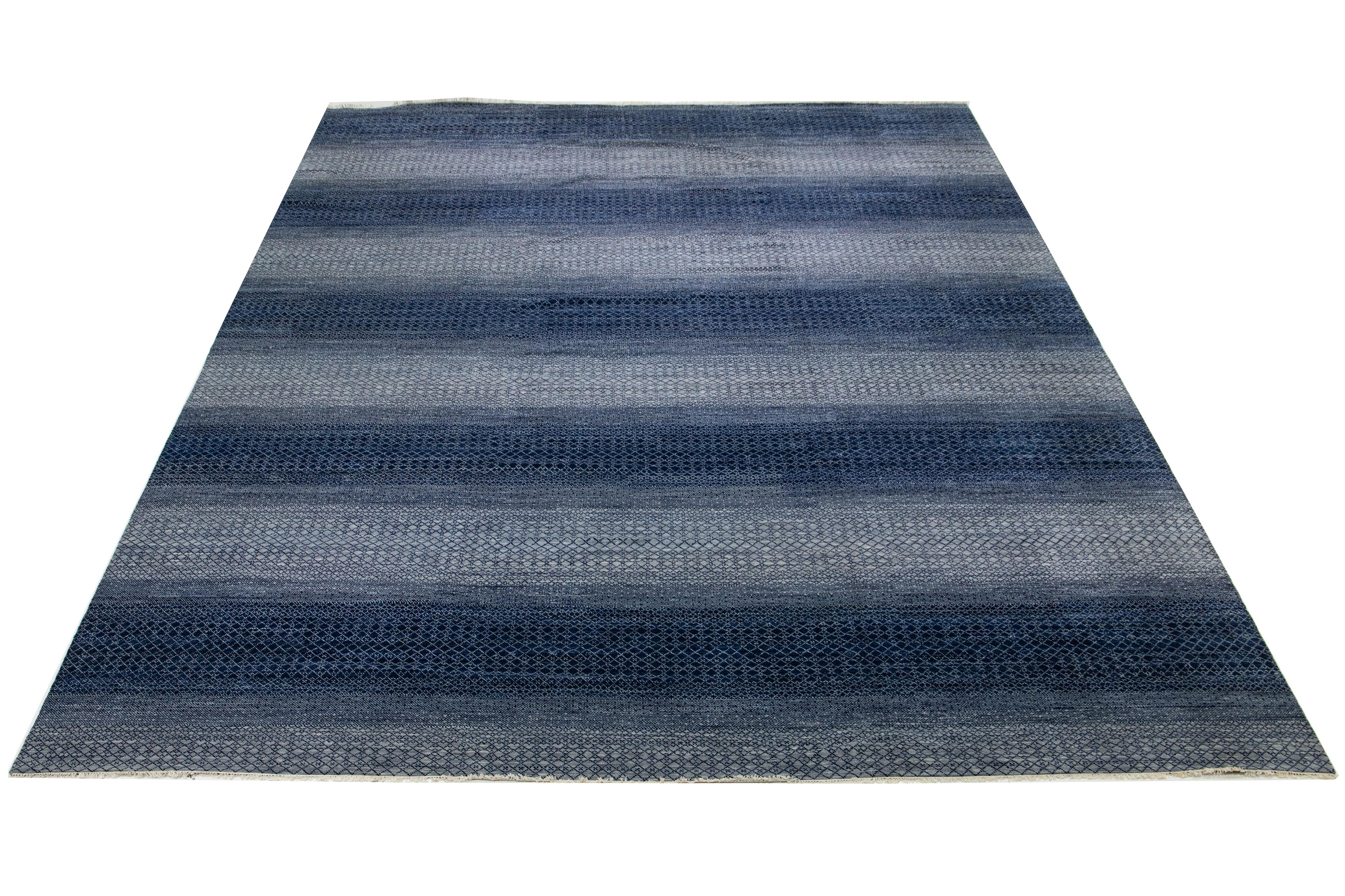 Ce tapis en laine surdimensionné noué à la main présente un design moderne caractérisé par un mélange de tons gris et bleu marine, complétés par des motifs géométriques.

Ce tapis mesure 16'2