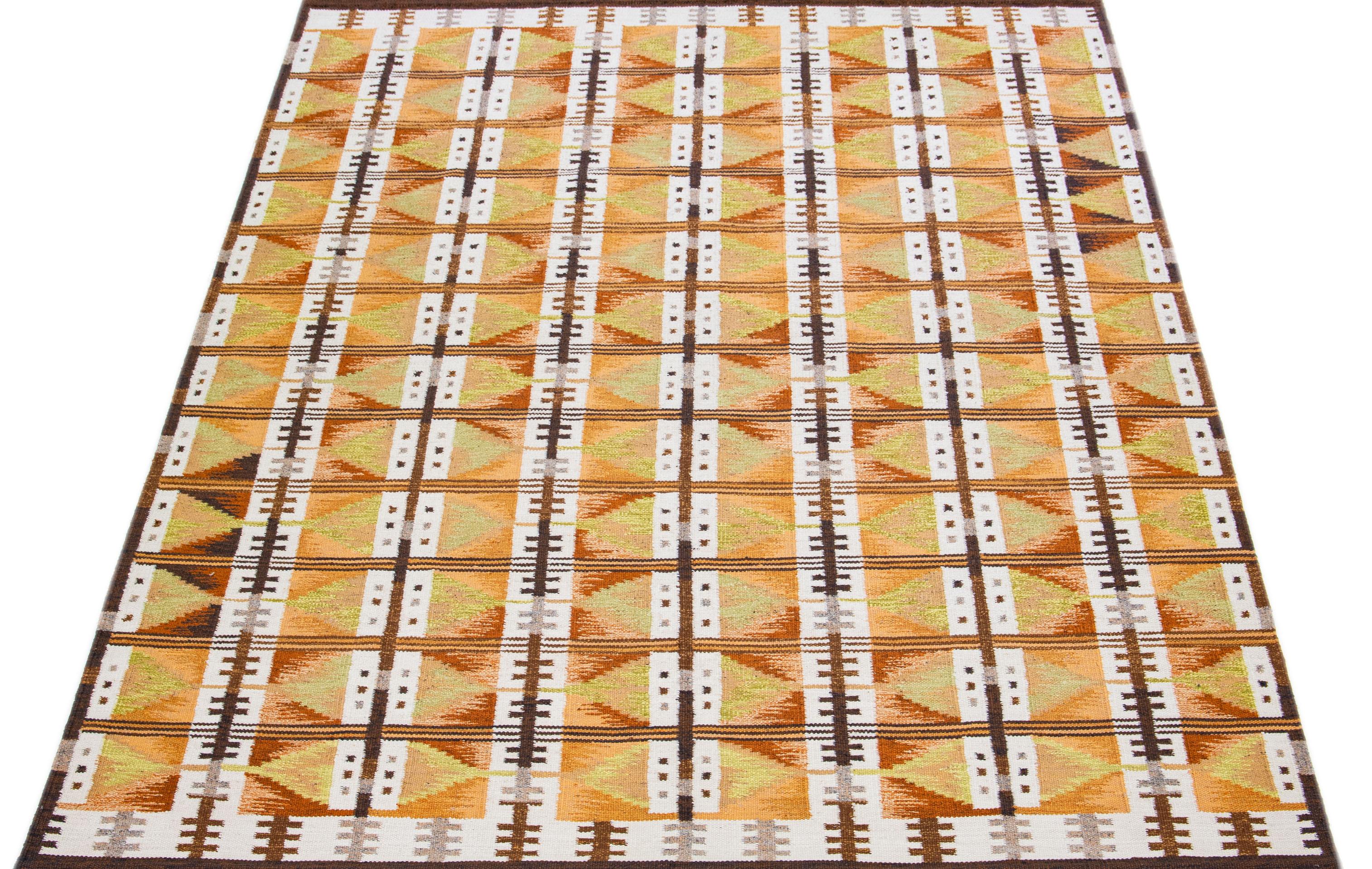 This contemporary woolen rug, showcasing a striking orange and brown base, seamlessly blends Nordic-inspired aesthetics with elegant geometric patterns featuring subtle green, gray, and ivory hints.

 This rug measures 9' x 12'3