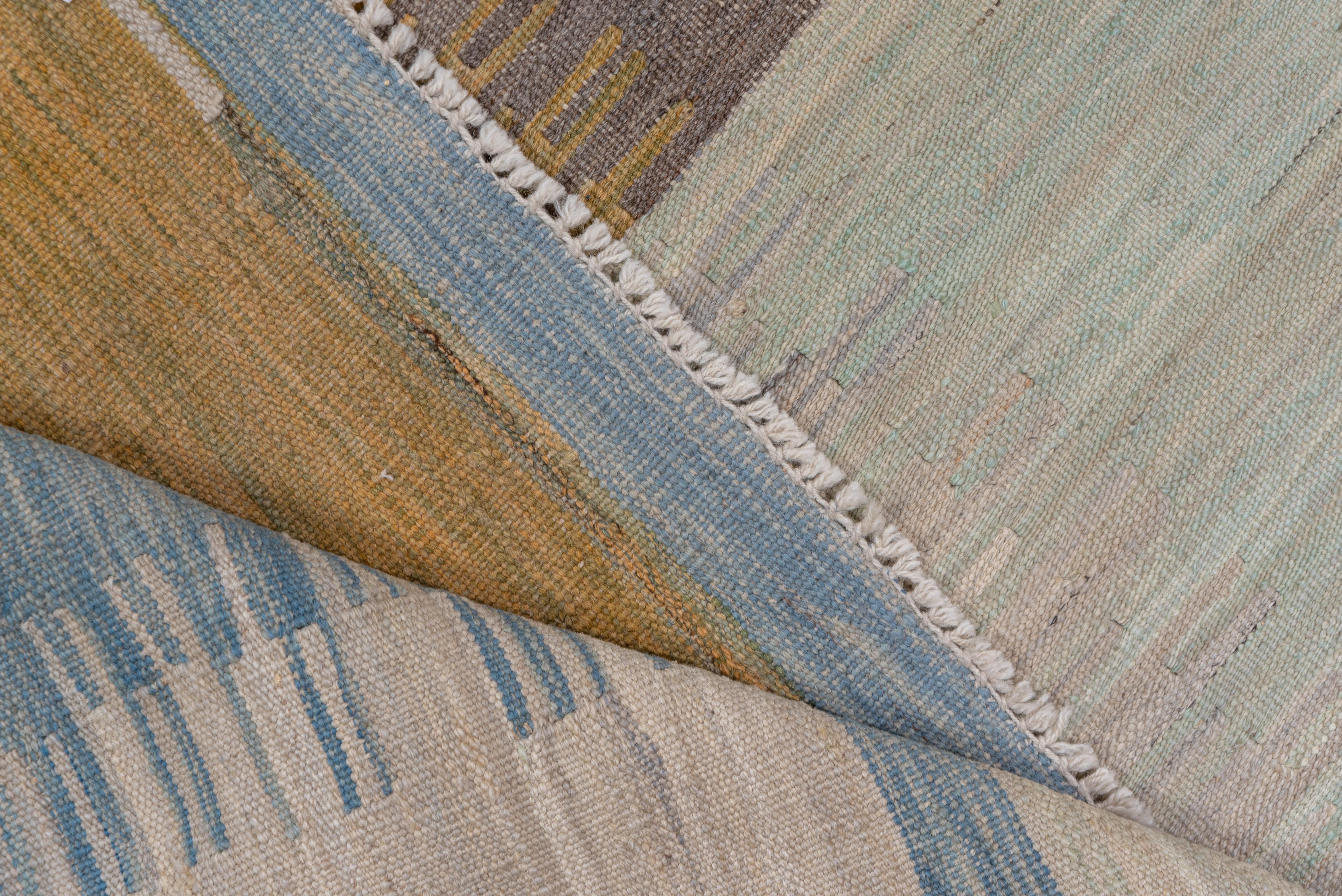 A nearly nine row pattern of variously fringed rectangles and squares gives a shimmering pattern of abrashed -light blue, brown, ivory and citron. The irregular comb edges show the color transitions with slit tapestry weave construction. As new