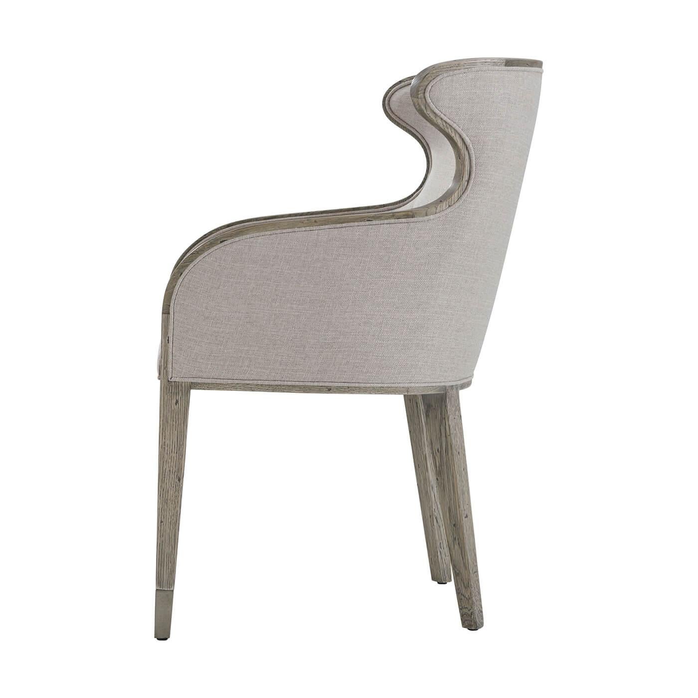 A modern scoop back upholstered dining chair with a greyed rustic oak finished frame, the organic wing back with a pierced handle and tight upholstered cushion seat, on square tapered legs with a textured vintage metal cap foot.

Dimensions: 23.5