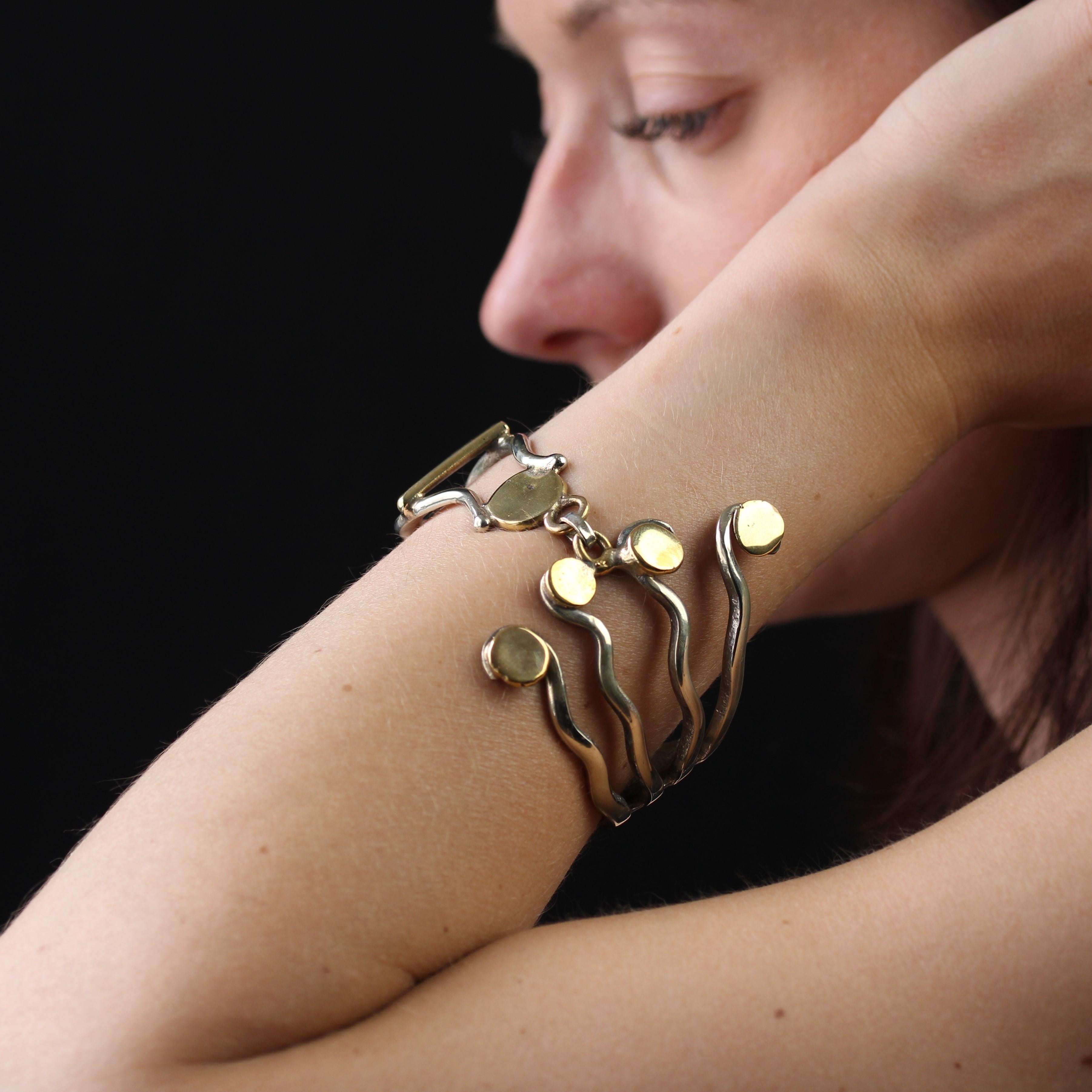 Bracelet in silver.
Original fork bracelet, the head is rounded to follow the movement of the wrist, the tines are spread out and form a wave, each ending in a gold-plated pastille. This part is articulated by an oval ring with the openwork fork