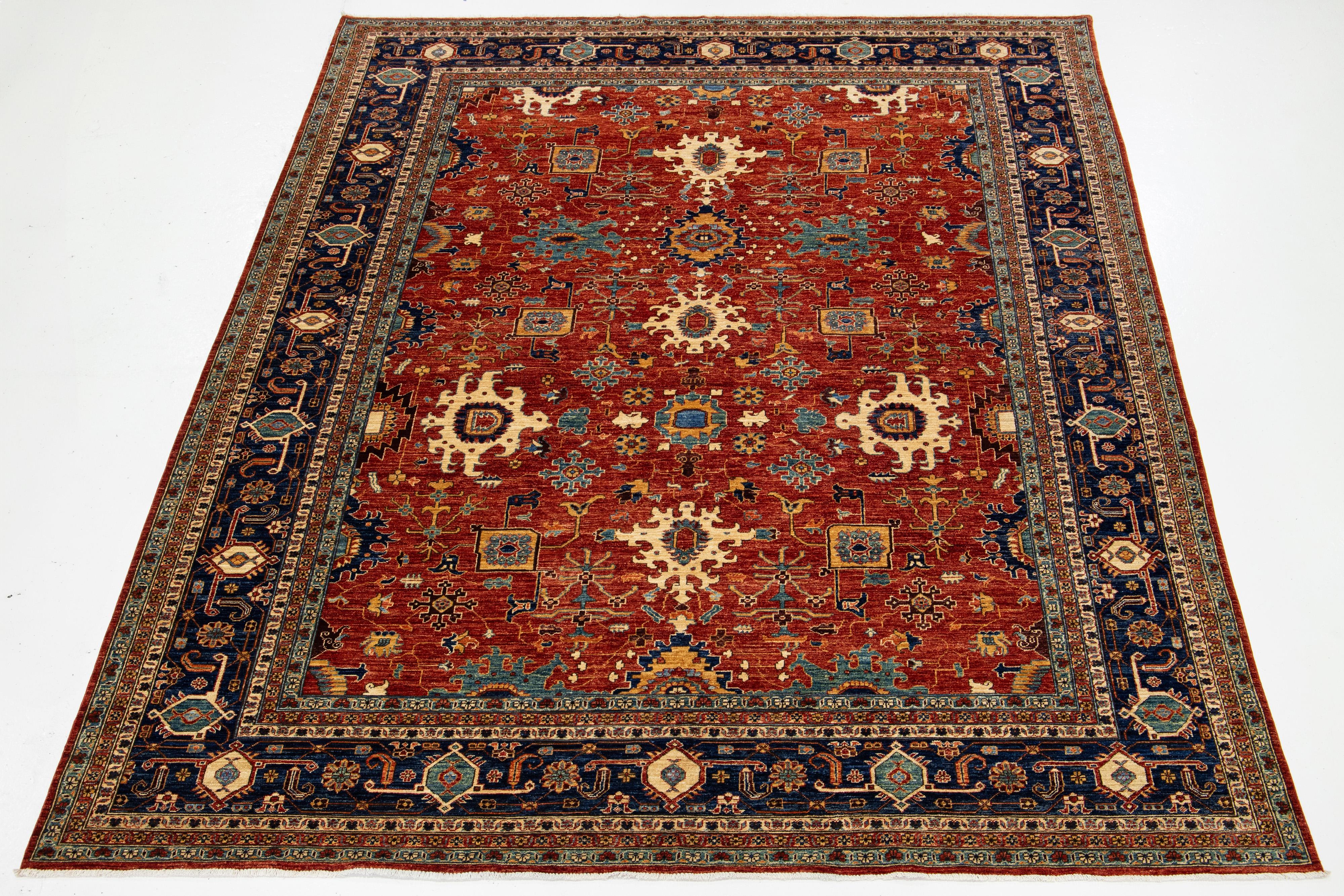 Dieser elegante Wollteppich zeigt einen klassischen, rostroten Hintergrund, der durch ein modernes, von Serapi inspiriertes Design ergänzt wird. Es hat einen akzentuierten Rahmen und ein wunderschönes florales Muster, das mit exquisiten mehrfarbigen